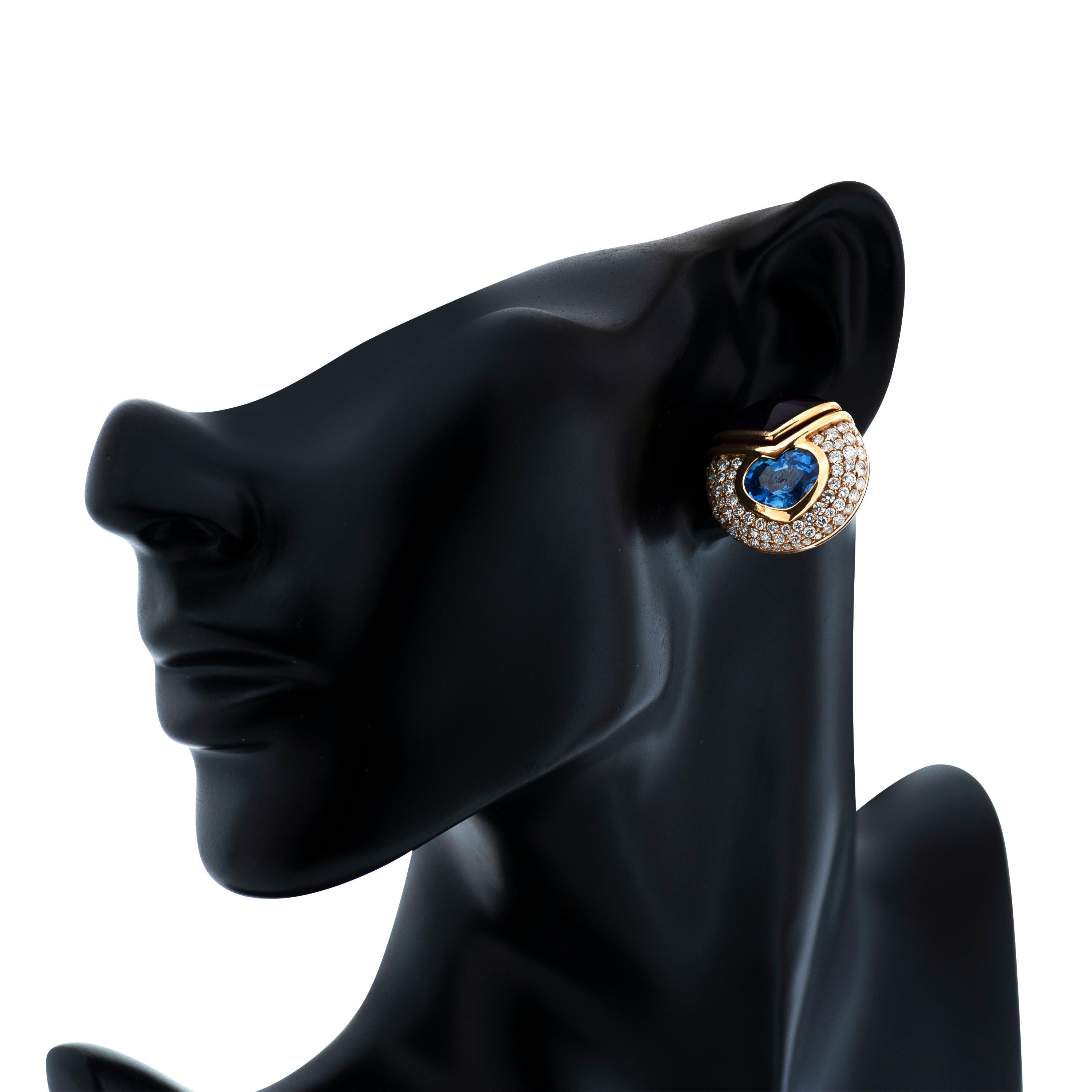 These vintage Bulgari earrings feature two blue and yellow heart shaped sapphires totaling approximately 14.45 carats bezel set in 18k yellow gold.  They are accented with two fancy shaped cabochon amethysts and approximately 3.75 carats of round