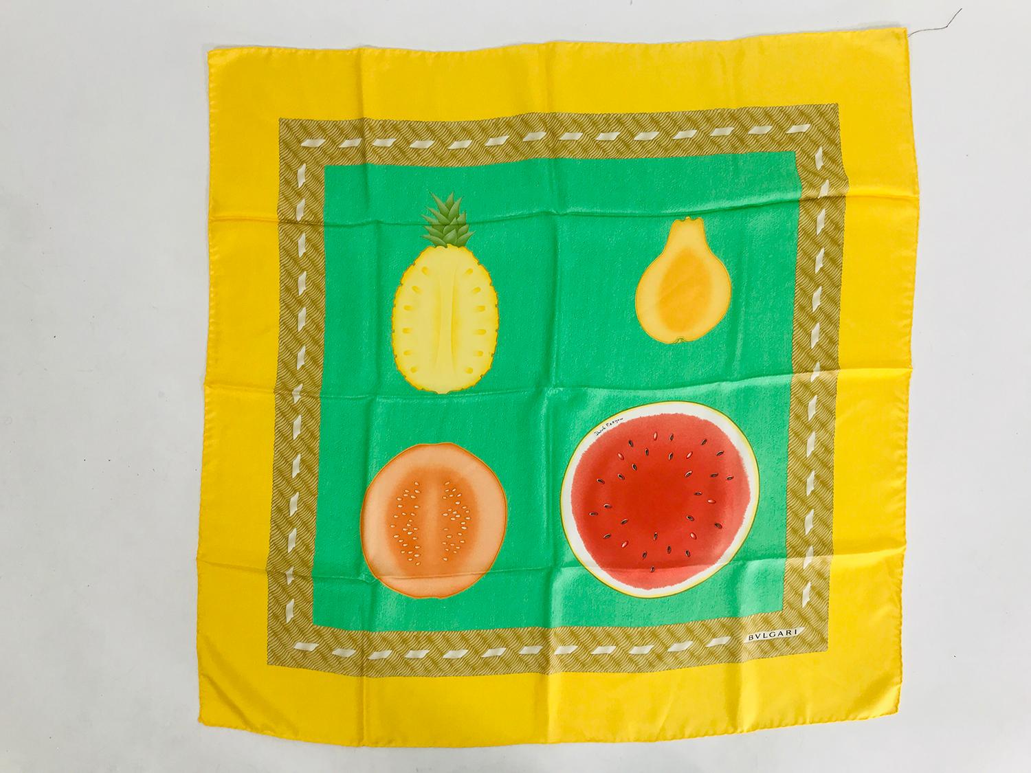 Bulgari colourful fruits silk scarf designed by Davide Pizzigoni. Bright yellow border with 4 large fruits set against a green ground,each in their own square. Surrounded with a tan with a braided border in taupes. This would be perfect to frame for