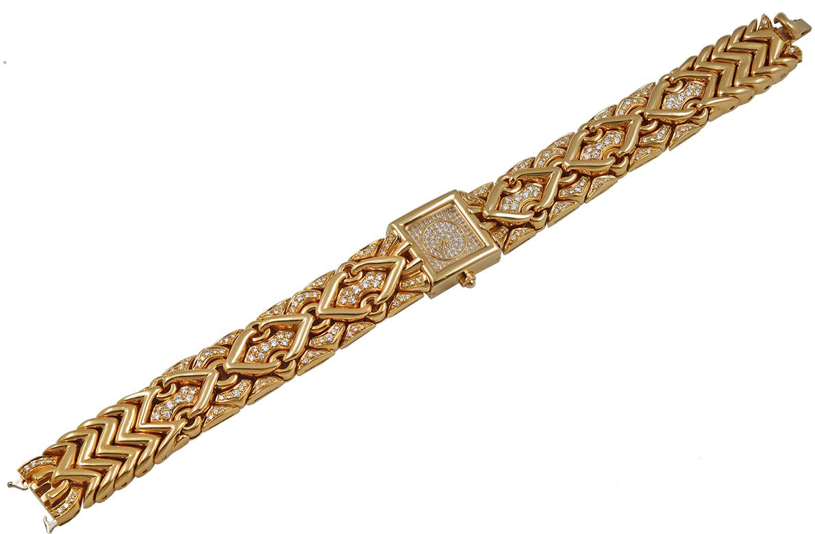 A magnificent 16mm Trika wrist watch by Bulgari, designed with a chatoyant chevron patterned band adorned by an opulence of pave diamonds finely crafted in 18k yellow gold. The square shaped dial exquisitely embellished with diamonds throughout. The