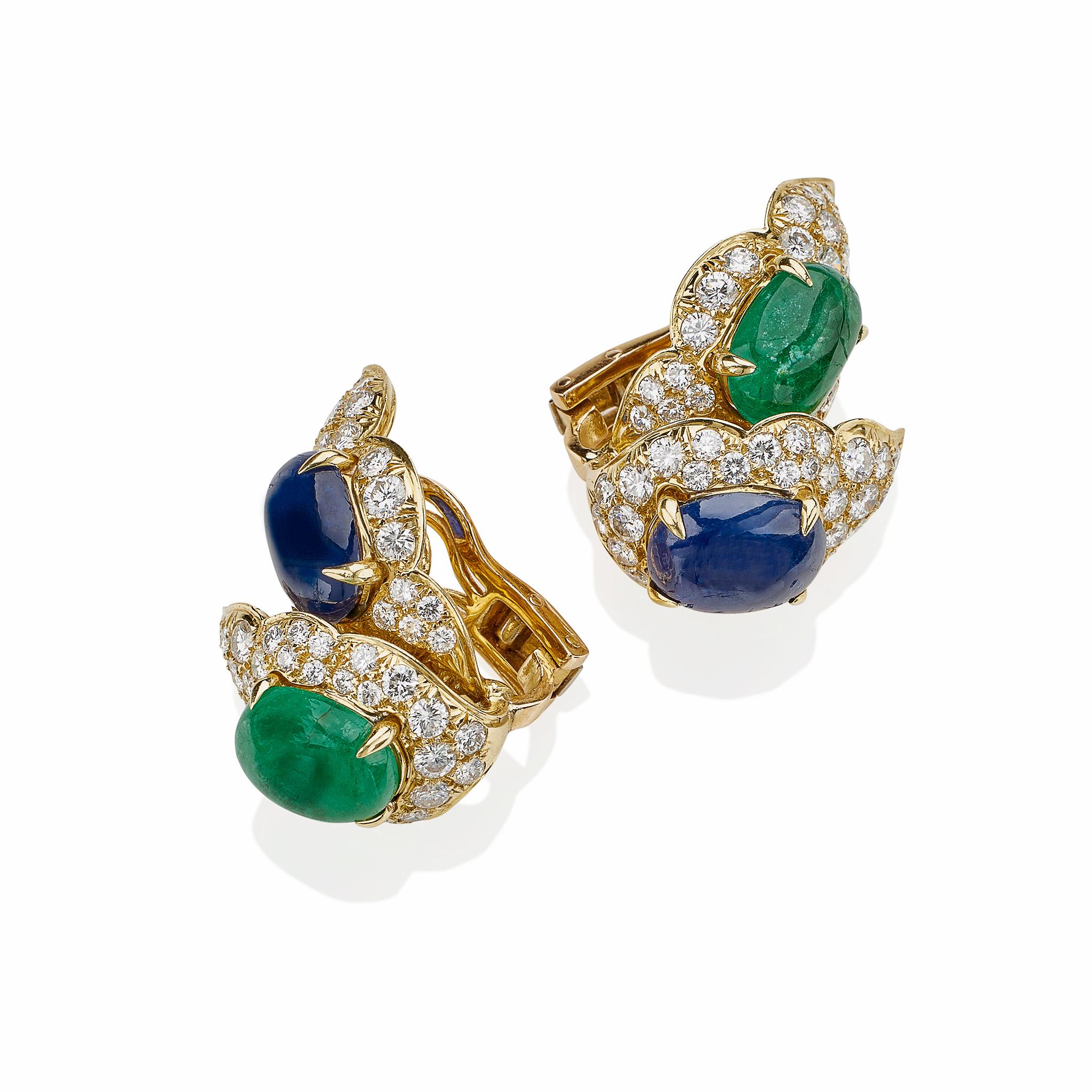 These 18K gold, emerald, sapphire and diamond clip earrings by Bulgari date from the 1980s. Designed as a double leaf forms, each leaf centers an oval cabochon emerald or sapphire framed by pavé-set round brilliant-cut diamonds, mounted in 18K gold.