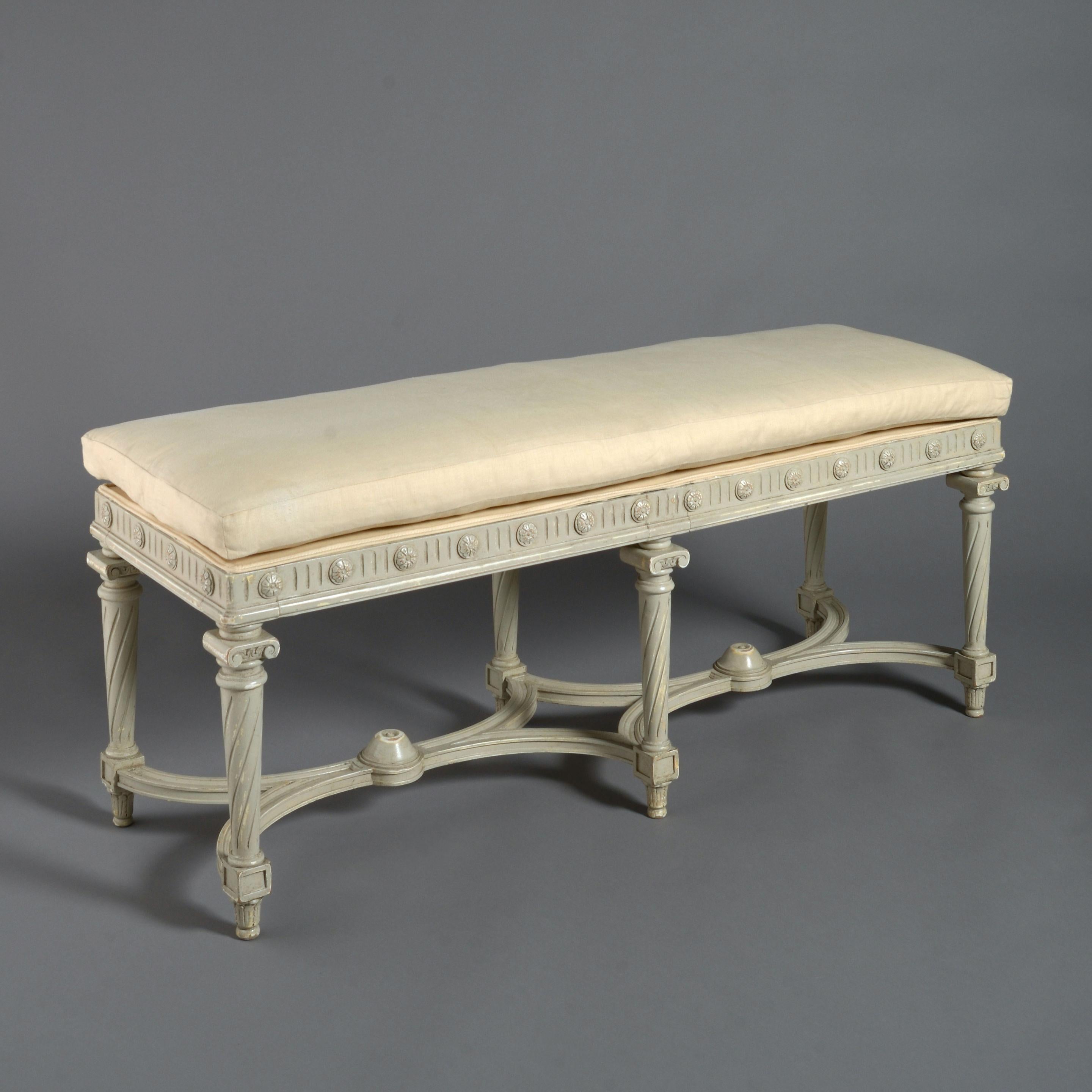 A late 19th century grey painted upholstered long stool in the Louis XVI style, a frieze of triglyphs and paterae set above six tapering spiral fluted column legs each headed with an ionic capital and all conjoined by concave stretchers. With a