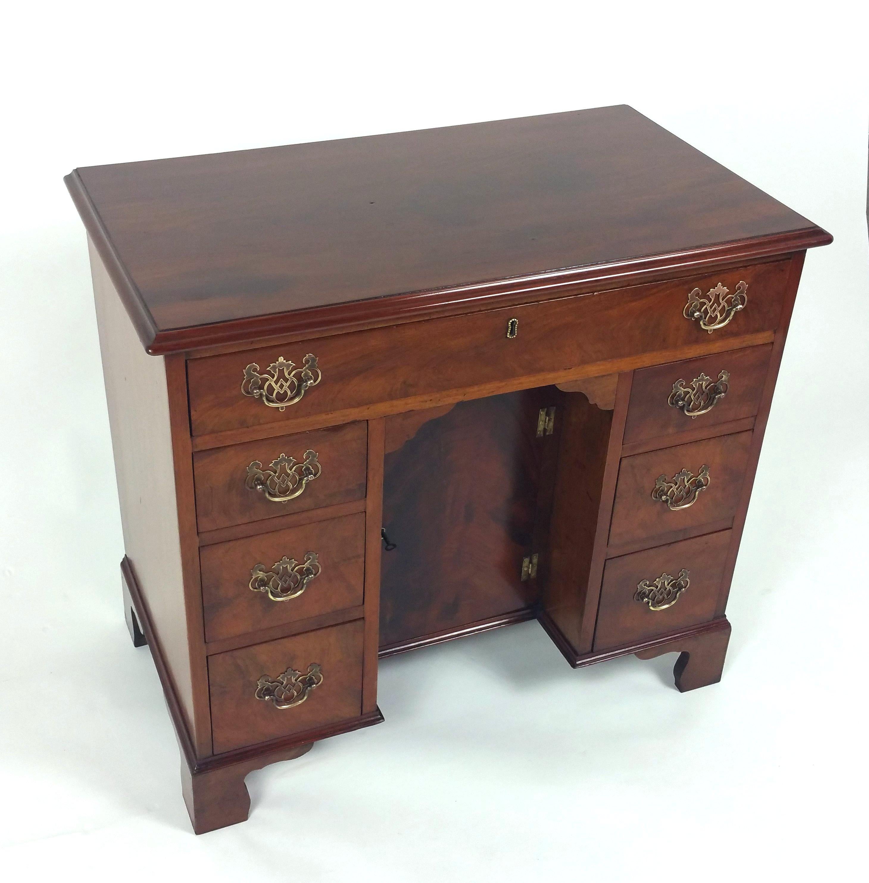 This attractive and well-proportioned George III mahogany knee hole desk features one long drawer over 6 smaller drawers and a central cupboard with lock and key. The desk stands on bracket feet and has the original and ornate pierced brass handles.