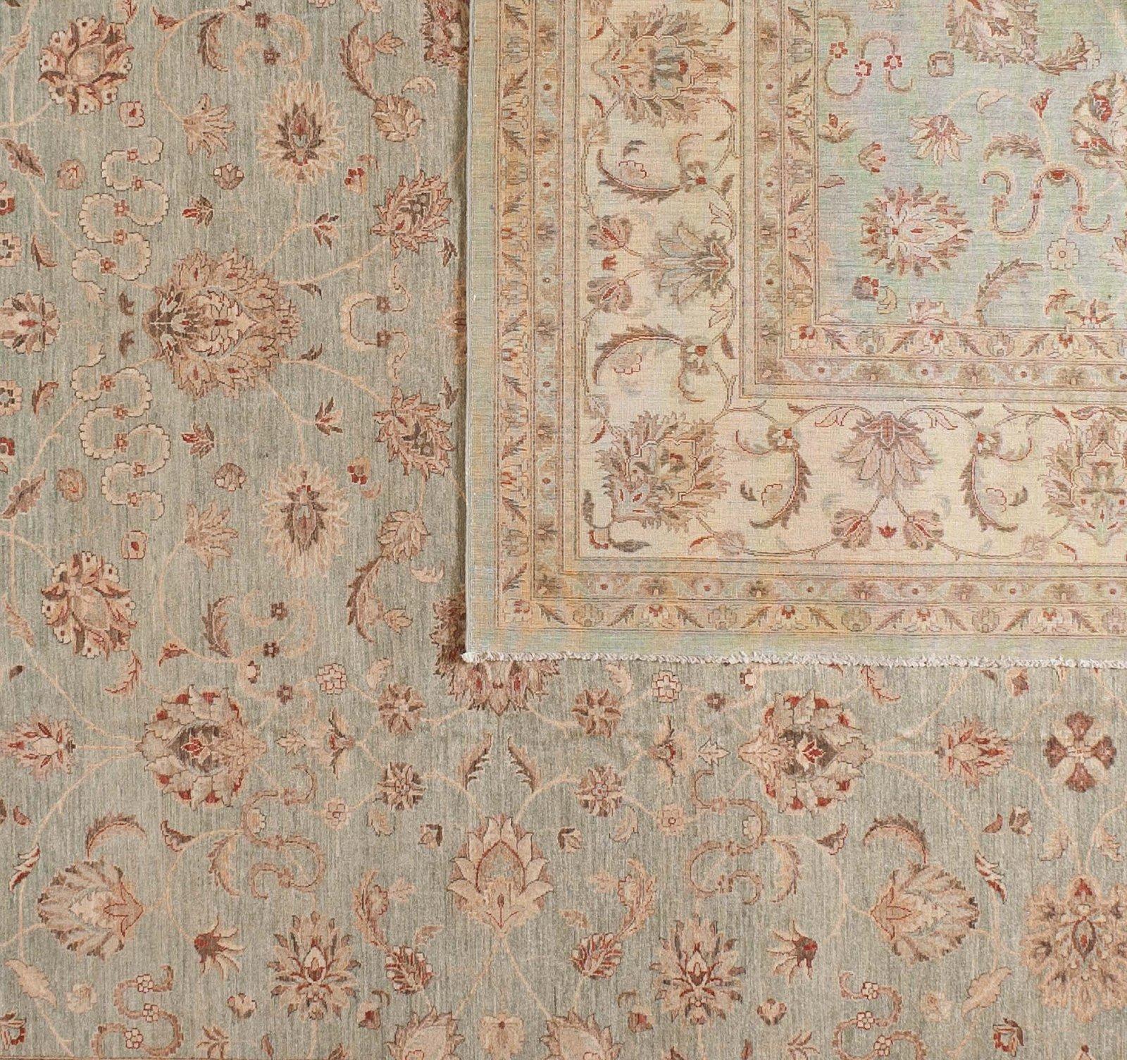Un motif floral complexe dans des tons pastel légers crée un tapis en laine chaleureux et élégant dans un style pakistanais traditionnel. Des fleurs et des vignes rouges, taupes, vertes foncées et jaunes s'étendent sur le panneau central vert clair