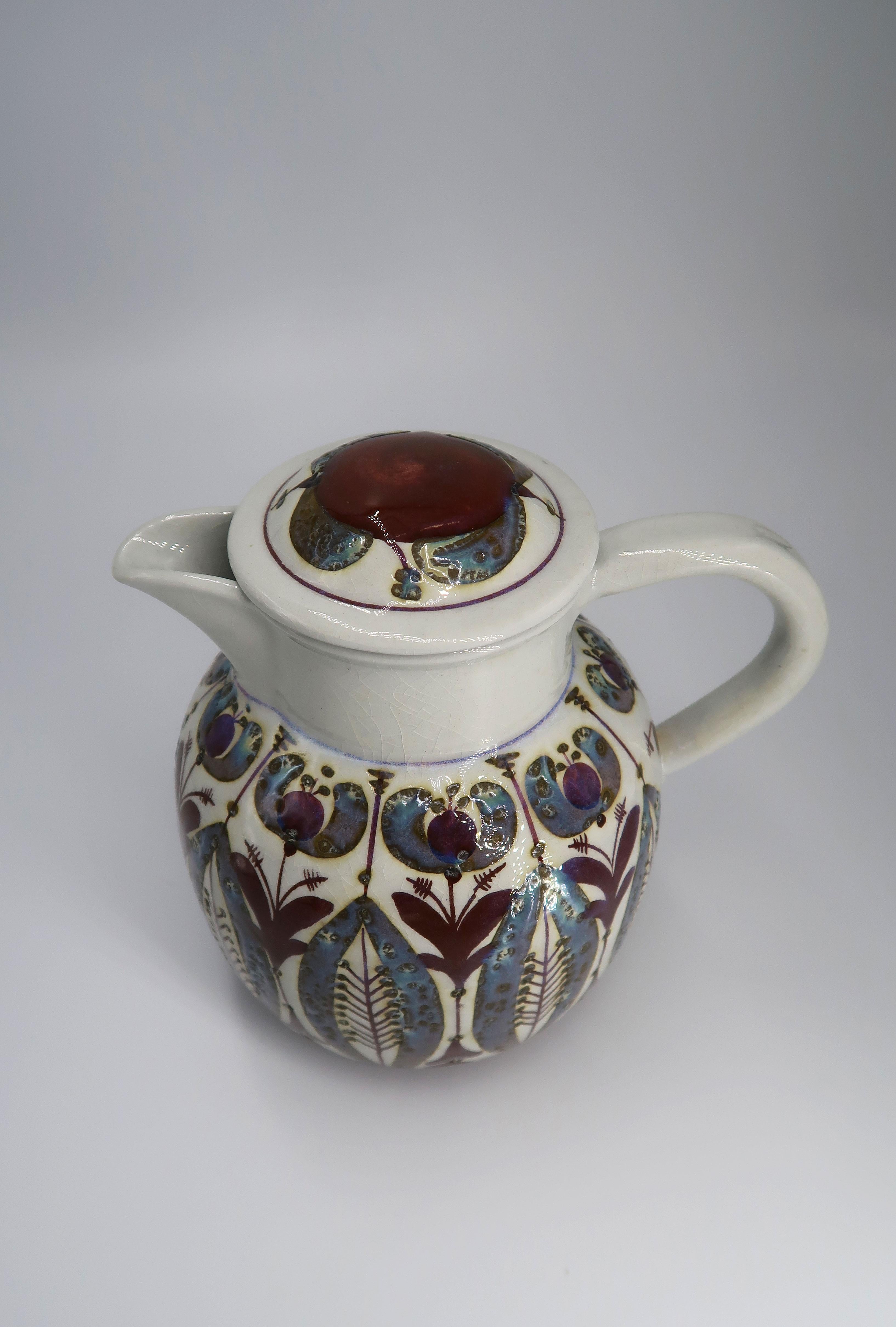 Beautiful Danish Mid-century Modern hand decorated faience pitcher by designer Berte Jessen for Royal Copenhagen. Hand painted organic decorations in plum, purple, blue and green. Manufactured by Royal Copenhagen in the early 1960s. Model 509/3143.