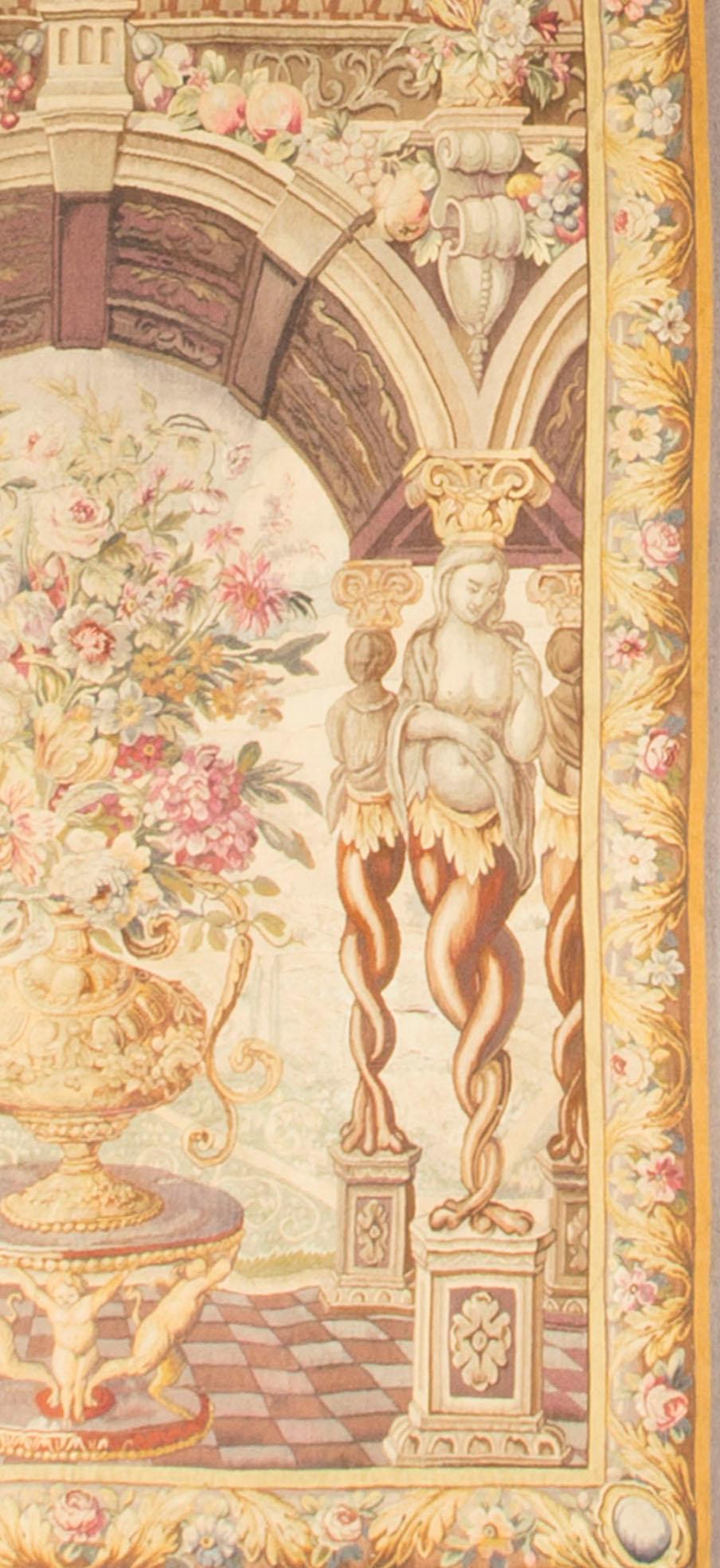 A French late 19th century copy, of a classical 17th century Flemish tapestry, depicting Nymphs holding up an arch, which is enclosing a magnificent porcelain pot, filled to brimming with the most exquisite flower arrangement. In front of the