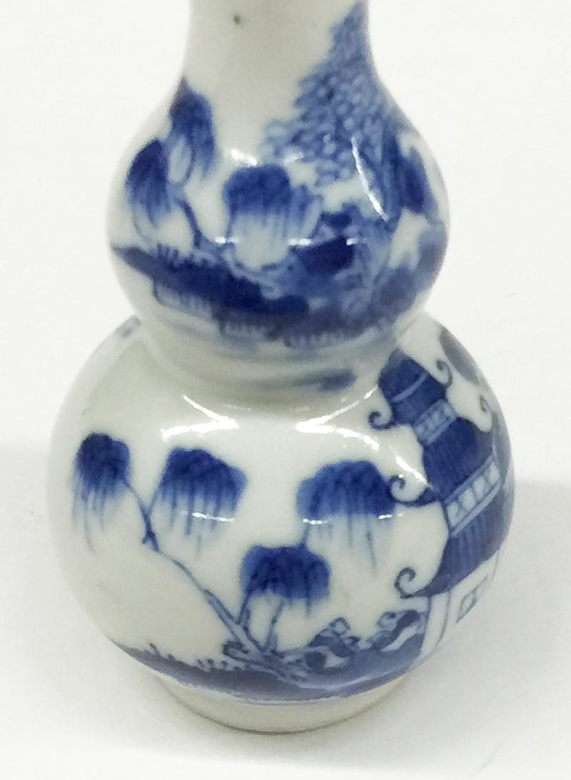 18th Century Chinese Blue and White Double-Gourd Small Porcelain Vase

A Chinese double- gourd blue and white porcelain vase with a scene of a landscape at water,  a house and two people standing on a bridge and one in front of the house and 2