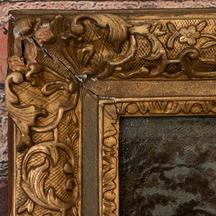 This naive landscape of a monastery perched on rocks with a monk fishing below, is unsigned and mounted in an ornate gilt wood and gesso frame. The painting has minor craquelure throughout the canvas and stretcher marks are visible, reflective of