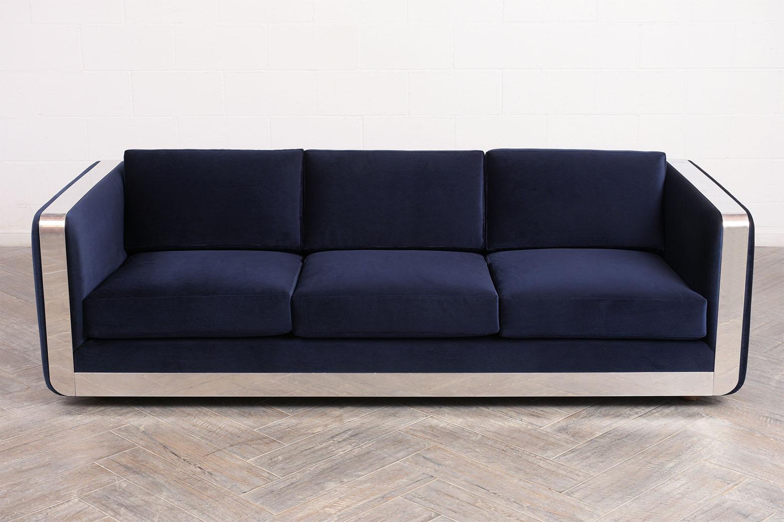 This 1960s stylish modern velvet sofa with chrome molding is in good condition. The sofa has been completely reupholstered comes with three comfortable seat cushions and three back pillows upholstered in a navy blue velvet fabric and with topstitch