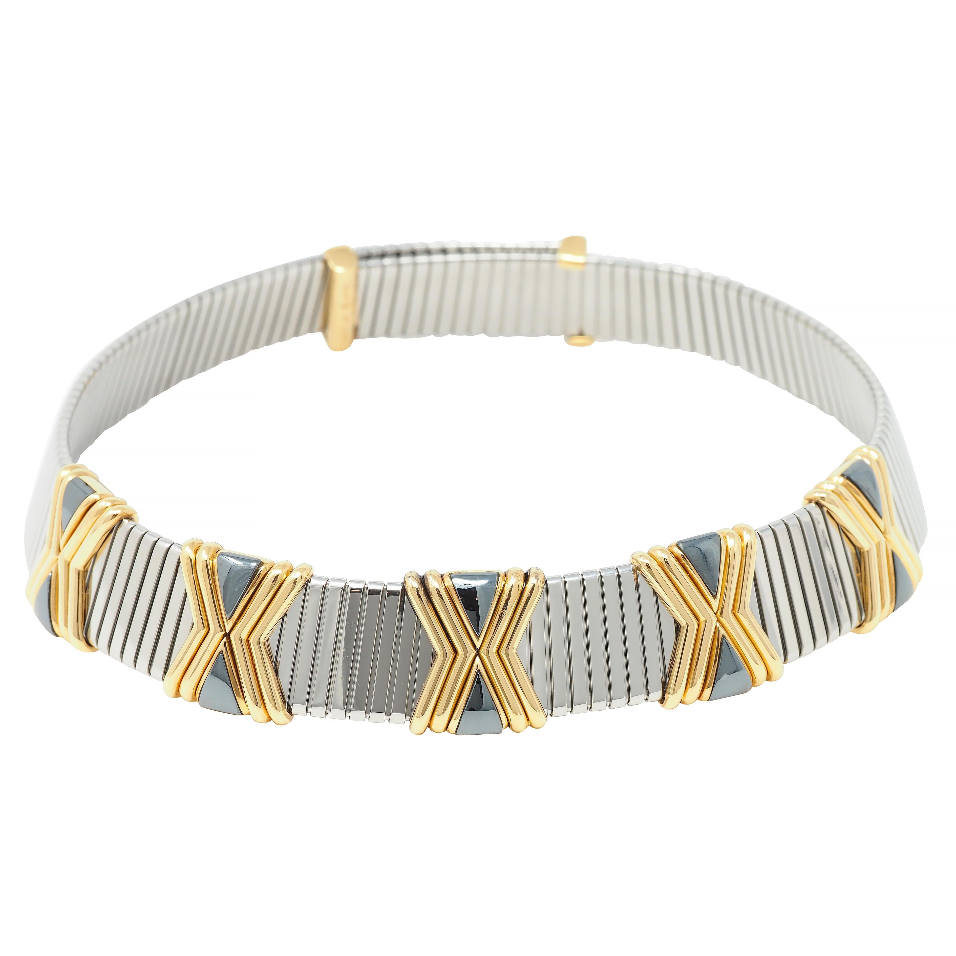 Comprised of grooved stainless steel segments with raised yellow gold 'X' motif stations 
Accented by triangular-shaped hematite inlay - dark metallic gray with gold surrounds
Tubogas style with considerable flexibility and movement 
Completed by