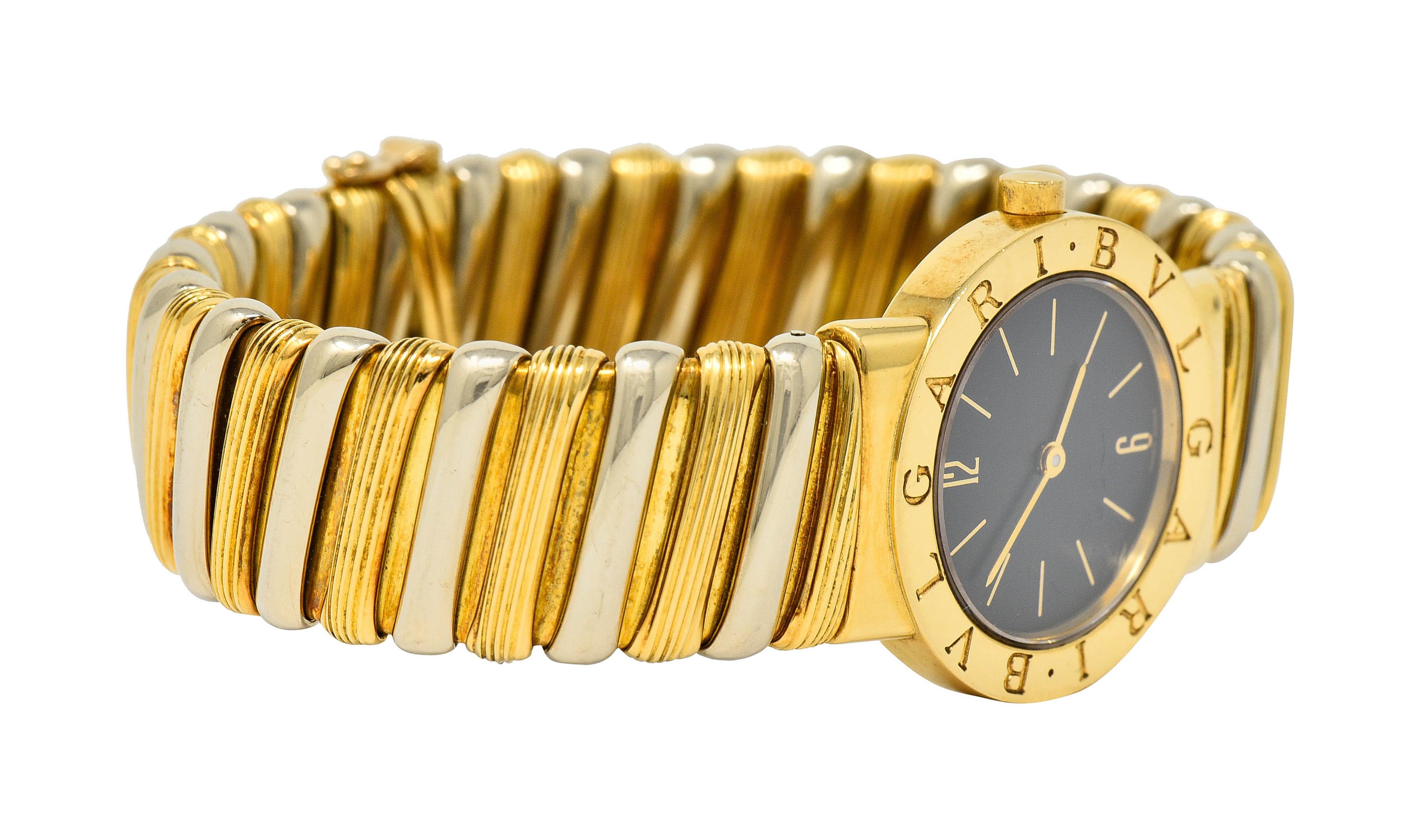Springy cuff bracelet is comprised of polished white gold links alternating with ribbed gold links

Centering a sapphire crystal cover over a black watch face accented by gold hands and numerical markers

With a polished gold surround deeply