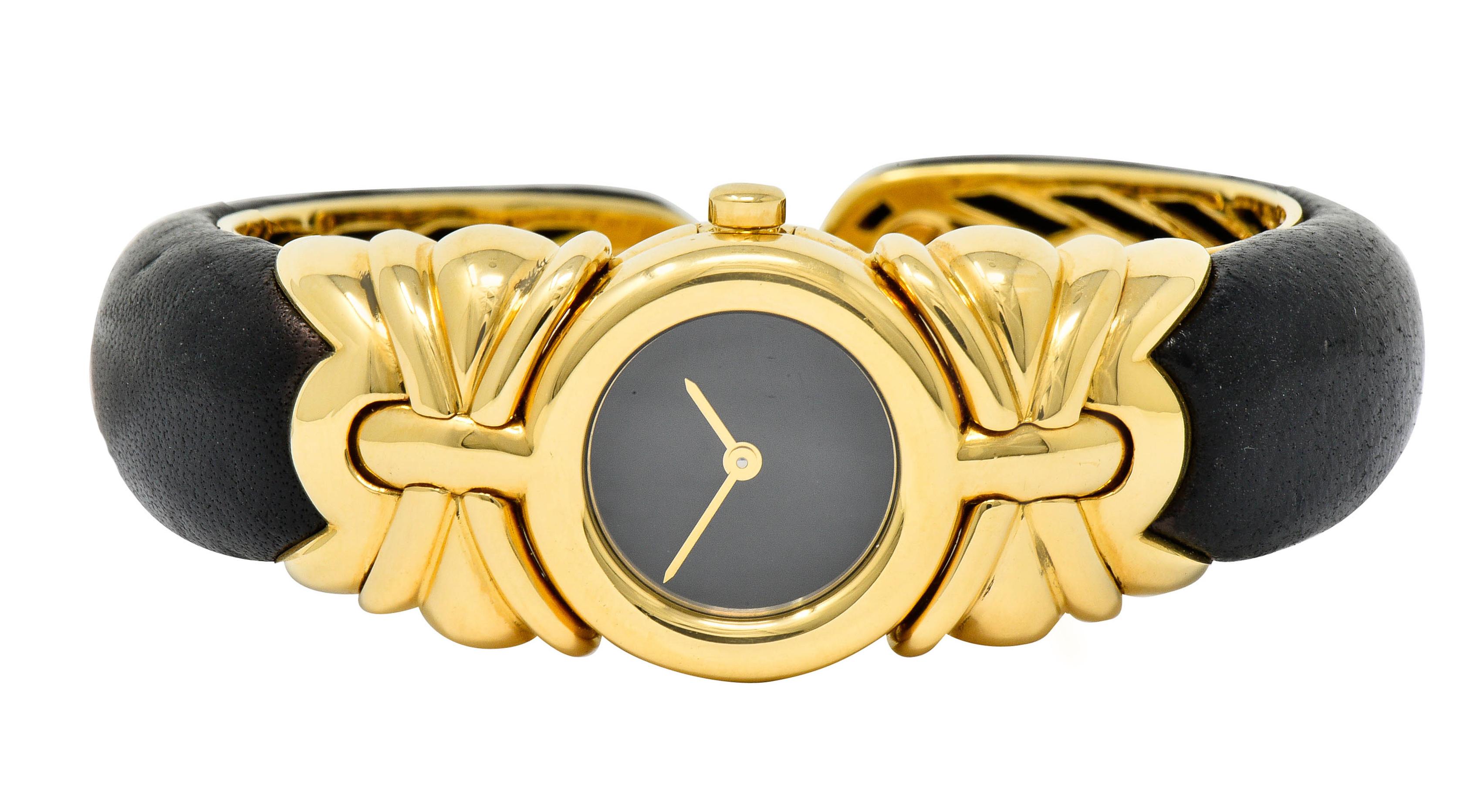 Centering a round sapphire crystal cover over a black watch face and polished gold hands

Surrounded by a polished gold circular bezel with gold crown

Flanked by stylized gold shoulders that complete as a black leather cuff

Cuff is backed by