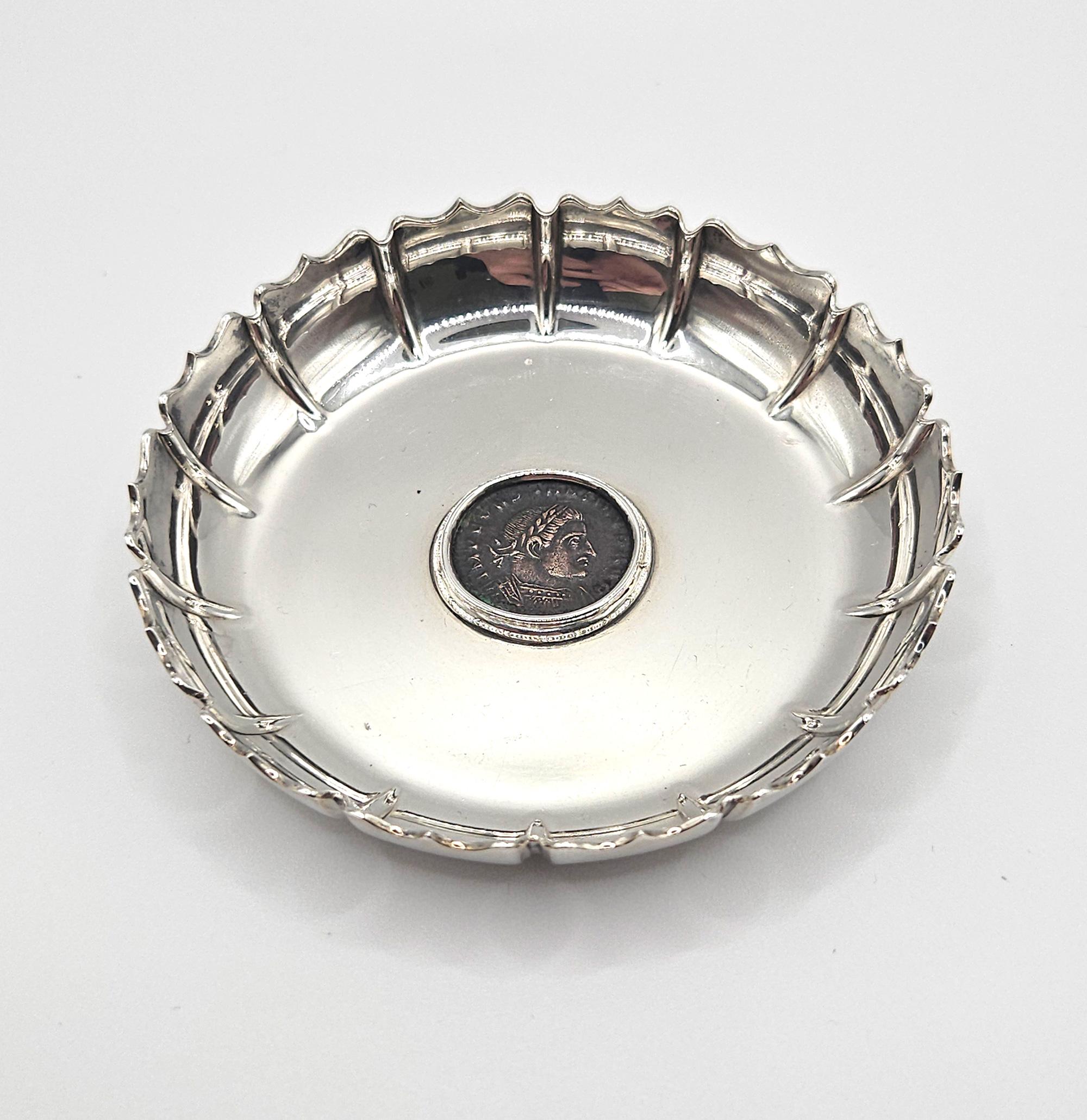 Un piatto o vide poche in argento 950 del Mid Century Antiques con una moneta greca antica al centro, realizzato da Bulgari nel 1970 circa. 

Il piatto ha una forma smerlata e reca il timbro 
