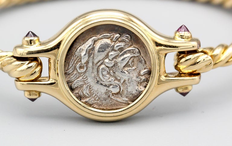 Fine and unusual 18K yellow gold, ruby, and ancient coin bangle bracelet, by Bulgari. It features an ancient Alexander the Great coin dating 336-323 A. C.  (Alessandro Magno, as written on the back of the coin bezel) .  The  bracelet further