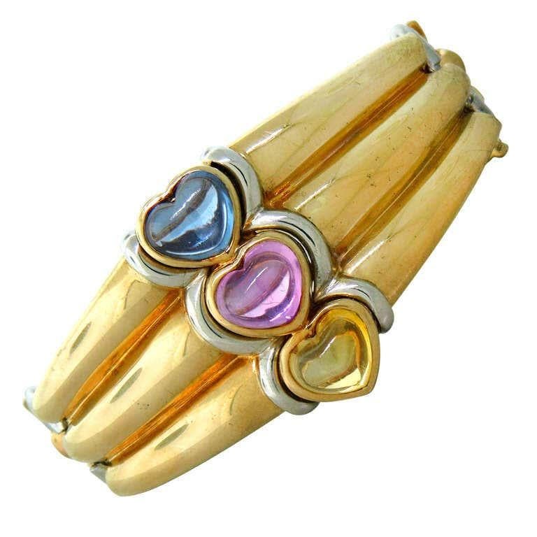 A chic cuff bracelet by Bulgari featuring three multi-color sapphire hearts set in two-color 18 karat gold. Made in Italy.
