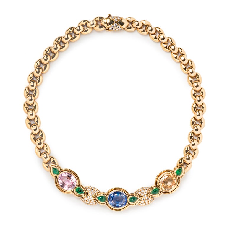Bulgari’s deft touch with color is fully realized in this necklace with matching ear clips. The 18k gold link necklace is set with three large faceted oval sapphires in pink, blue and yellow. Bright green cabochon emeralds nestle between them and