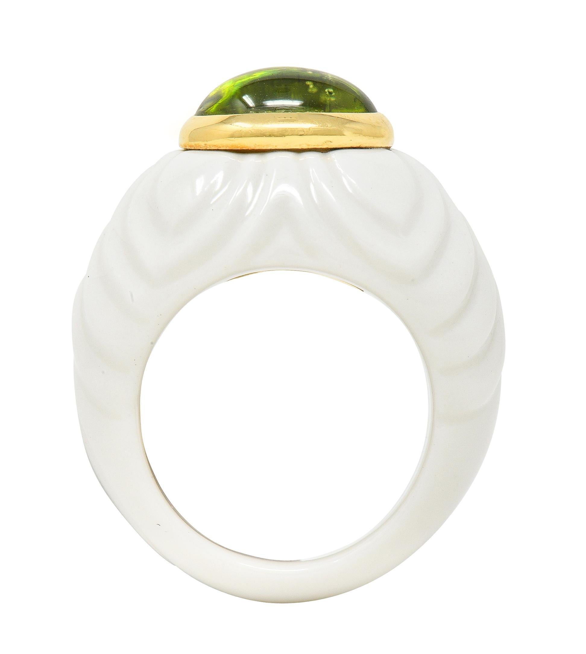 Centering an oval-shaped peridot cabochon measuring 7.5 x 10.0 mm 
Bezel set east to west and transparent medium yellowish green
Set atop a domed ceramic form with grooved petal motif 
Opaque glossy white in color
Stamped with Italian assay marks