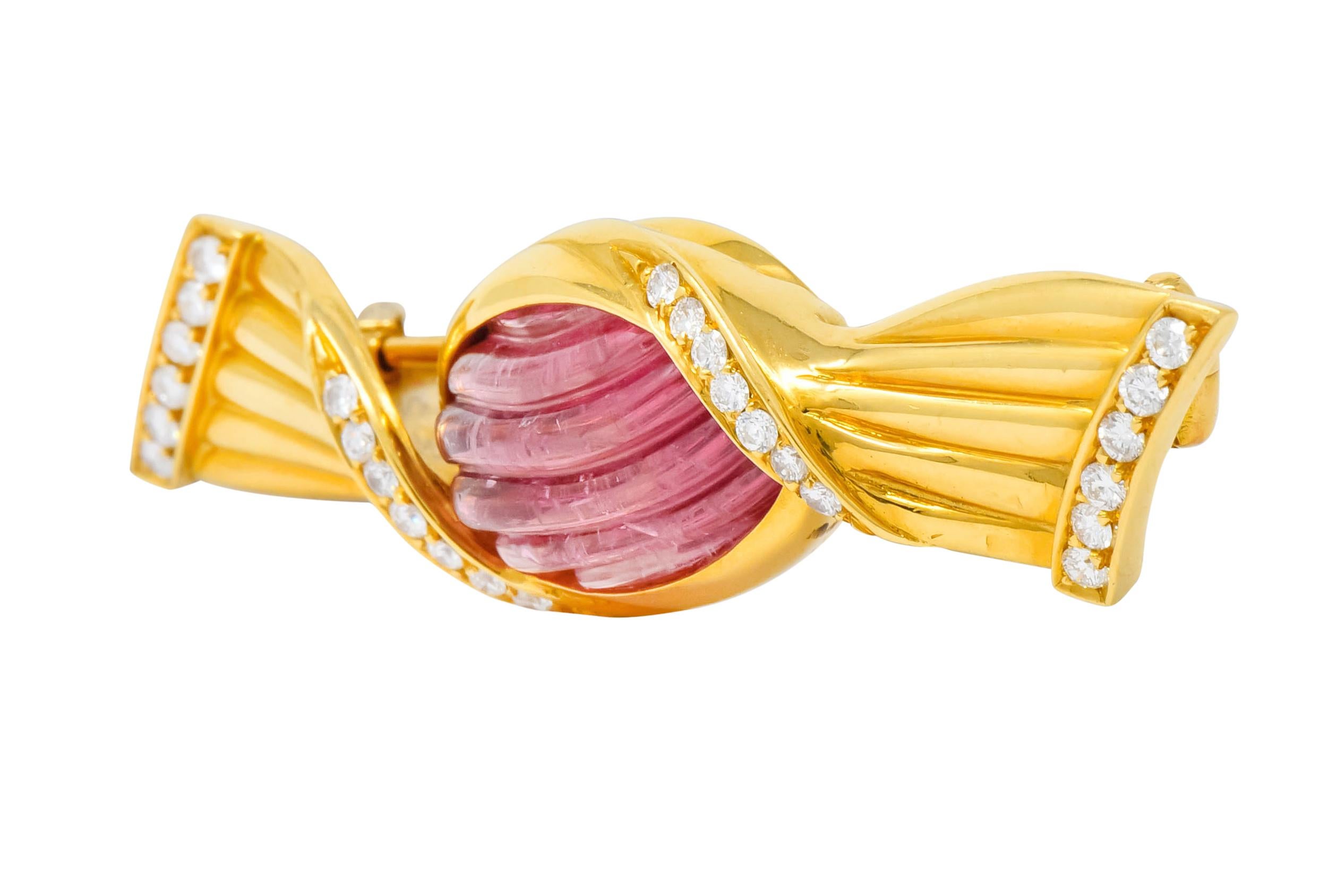Brooch designed as a colorful hard candy in a polished gold wrapper, twisted and deeply ridged

Centering an oval cabochon pink tourmaline with deeply carved fluting, measuring approximately 13.5 x 10.0 mm

Accented by round brilliant cut diamonds