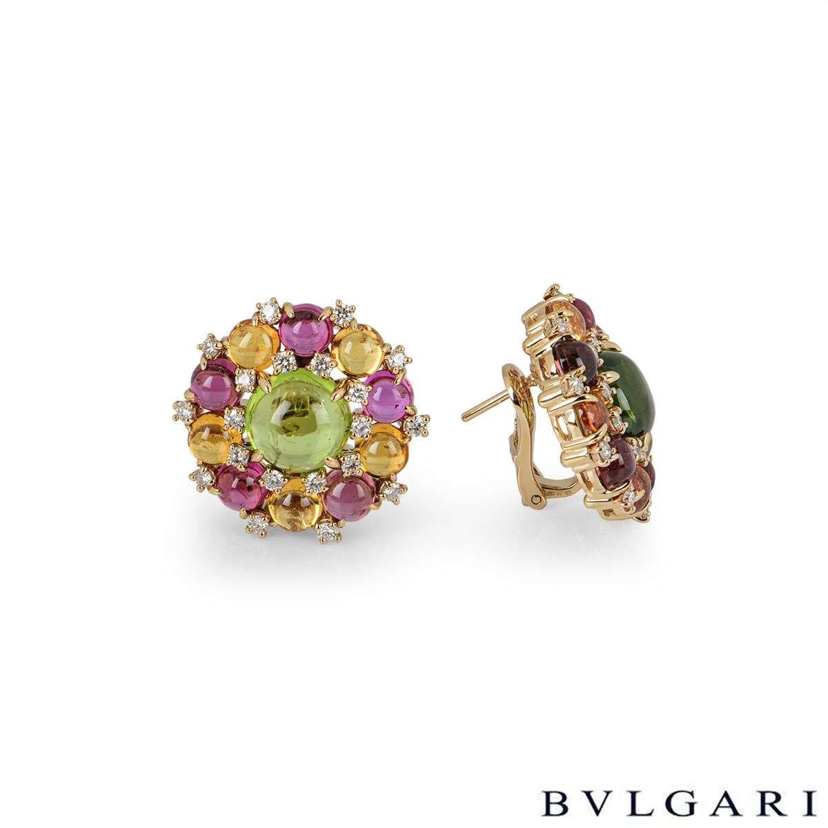A pair of 18k rose gold diamond and multi-gemstone earrings. The earrings each have a boarder of 10 alternating cabochon cut citrine and tourmaline gemstones, with a large peridot in the centre. There are 20 round brilliant cut diamonds set
