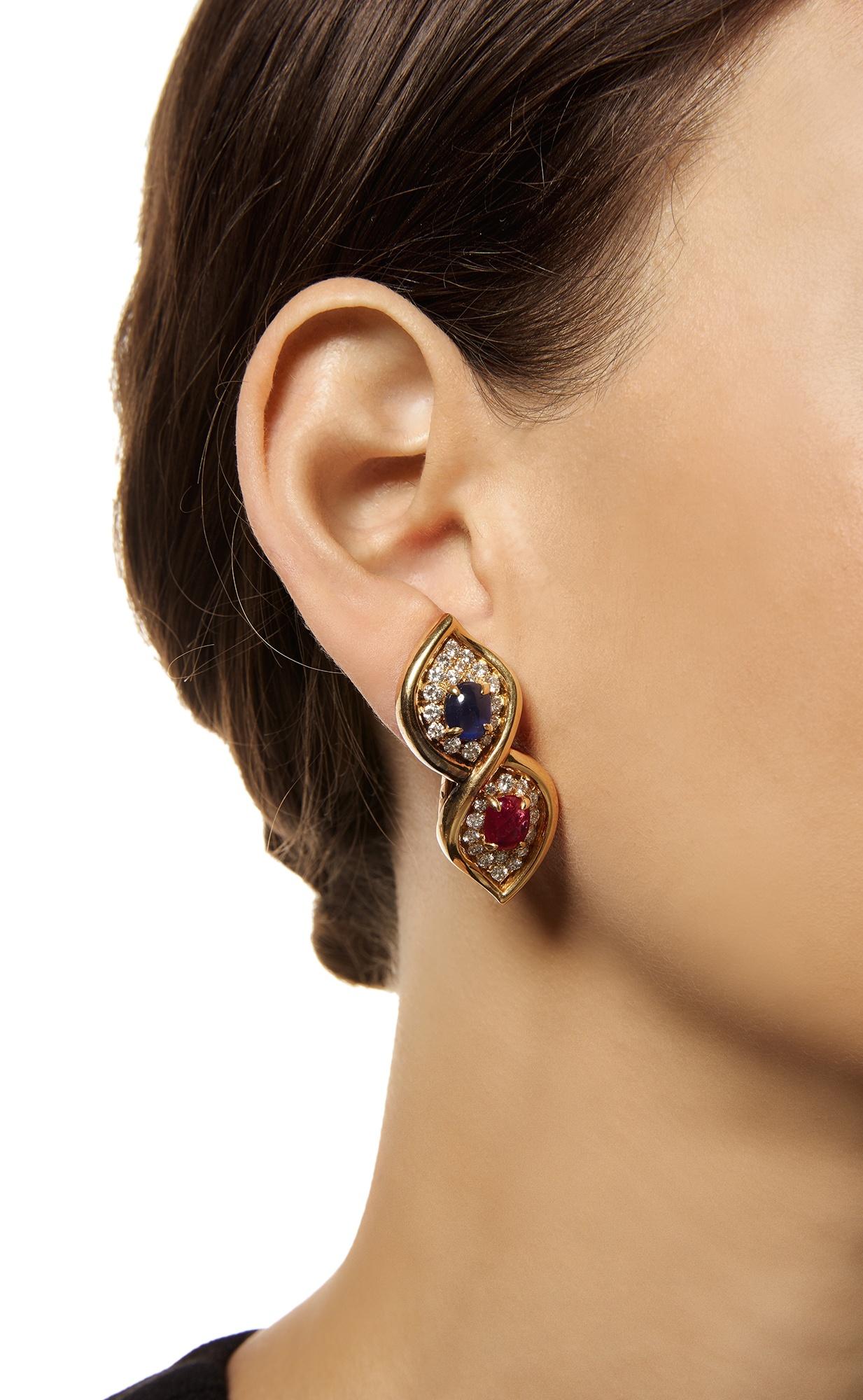 A Pair of Ruby, Sapphire and Diamond Earclips by Bulgari. Made in Italy, circa 1970.
Set with cabochon rubies and sapphires, encircled by pavé-set round diamonds, within polished gold figure eight frames.