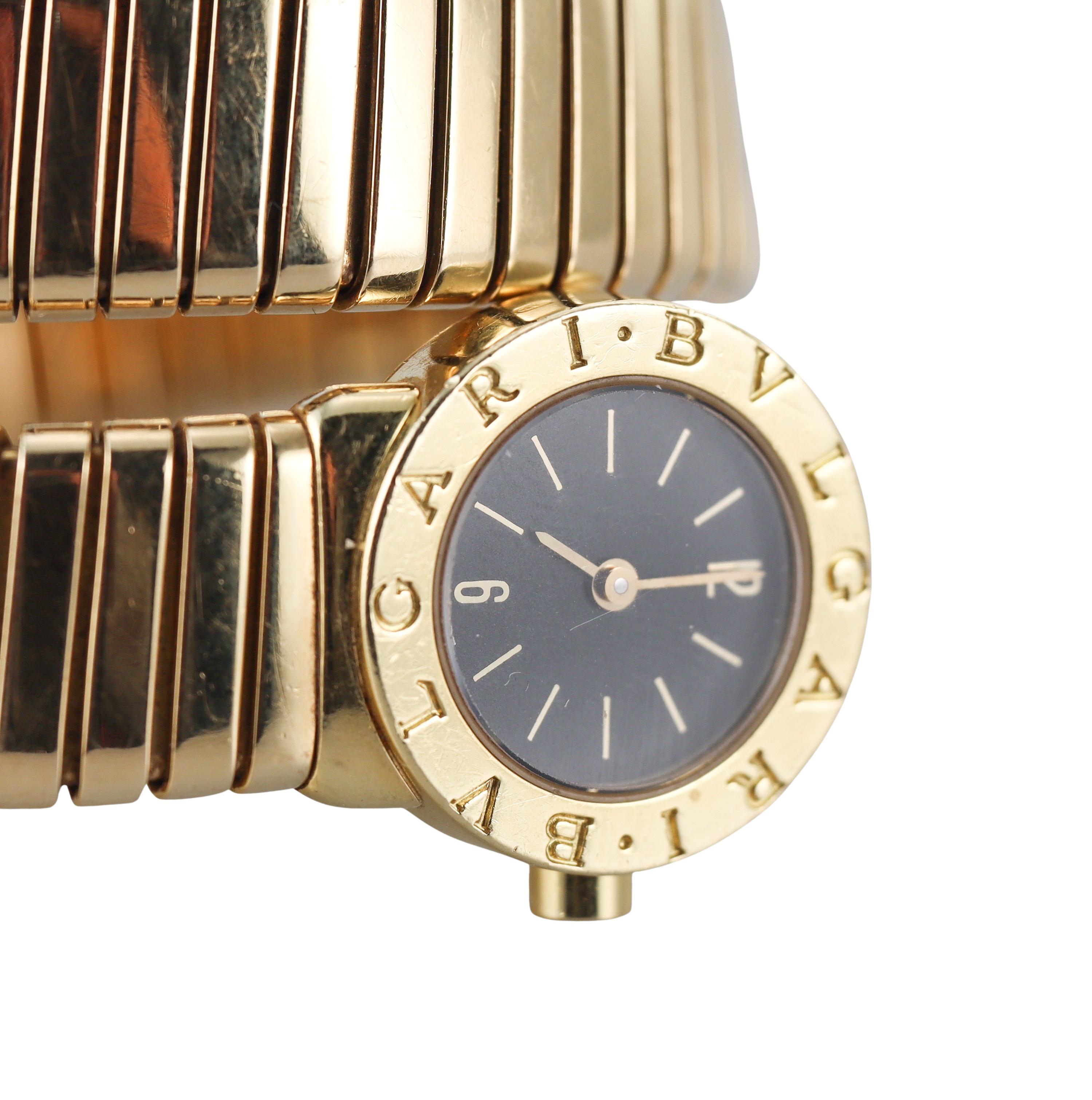Classic 18k yellow gold wrap Tubogas watch by Bvlgari, featuring black dial with applied gold stick markers. The bracelet is slightly flexible, will comfortably  fit a small size wrist ( approx. 6-6.5