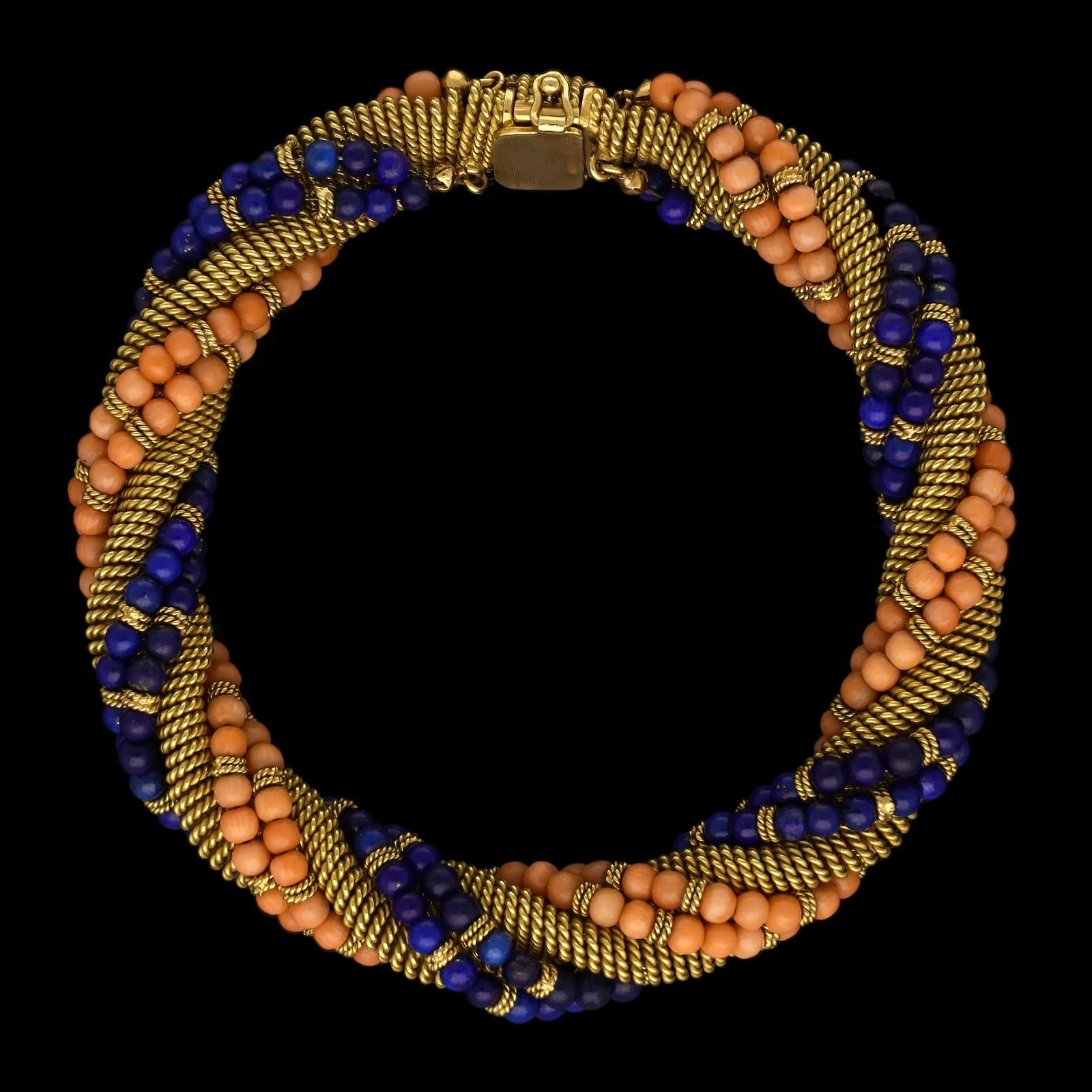 An unusual gold, coral and lapis lazuli bracelet by Bulgari c.1960, the bracelet formed of a woven gold strap twisted around and wrapped with a double row of round polished coral beads and another of matching lapis lazuli beads, the rows of beads