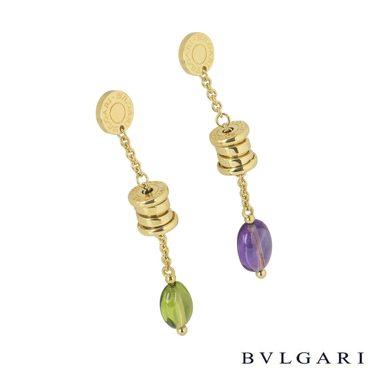 An 18k yellow gold pair of multi-gem earrings by Bvlgari from the B.zero1 collection. The earrings each comprise of the iconic 'Bvlgari Bvlgari' motif disc with the Bvlgari drum suspended from it and suspended from the barrel is a single peridot on