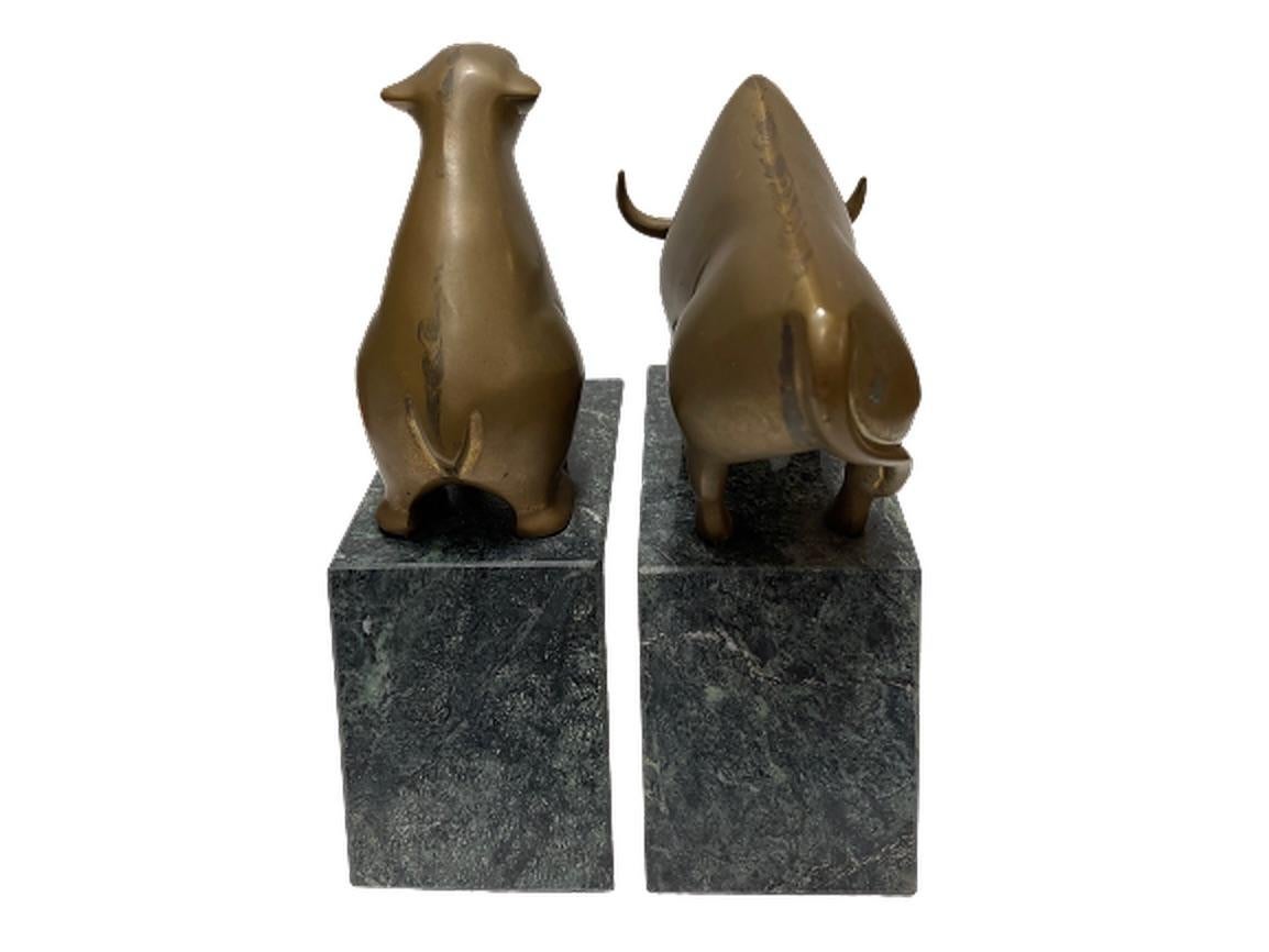 A pair of heavy marble bookends featuring a bull and bear, icons of the stock market and Wall Street. Both the bull and bear figures are made up of bronze. The bases are a deep, green marble. This is a statement piece for displaying your collection