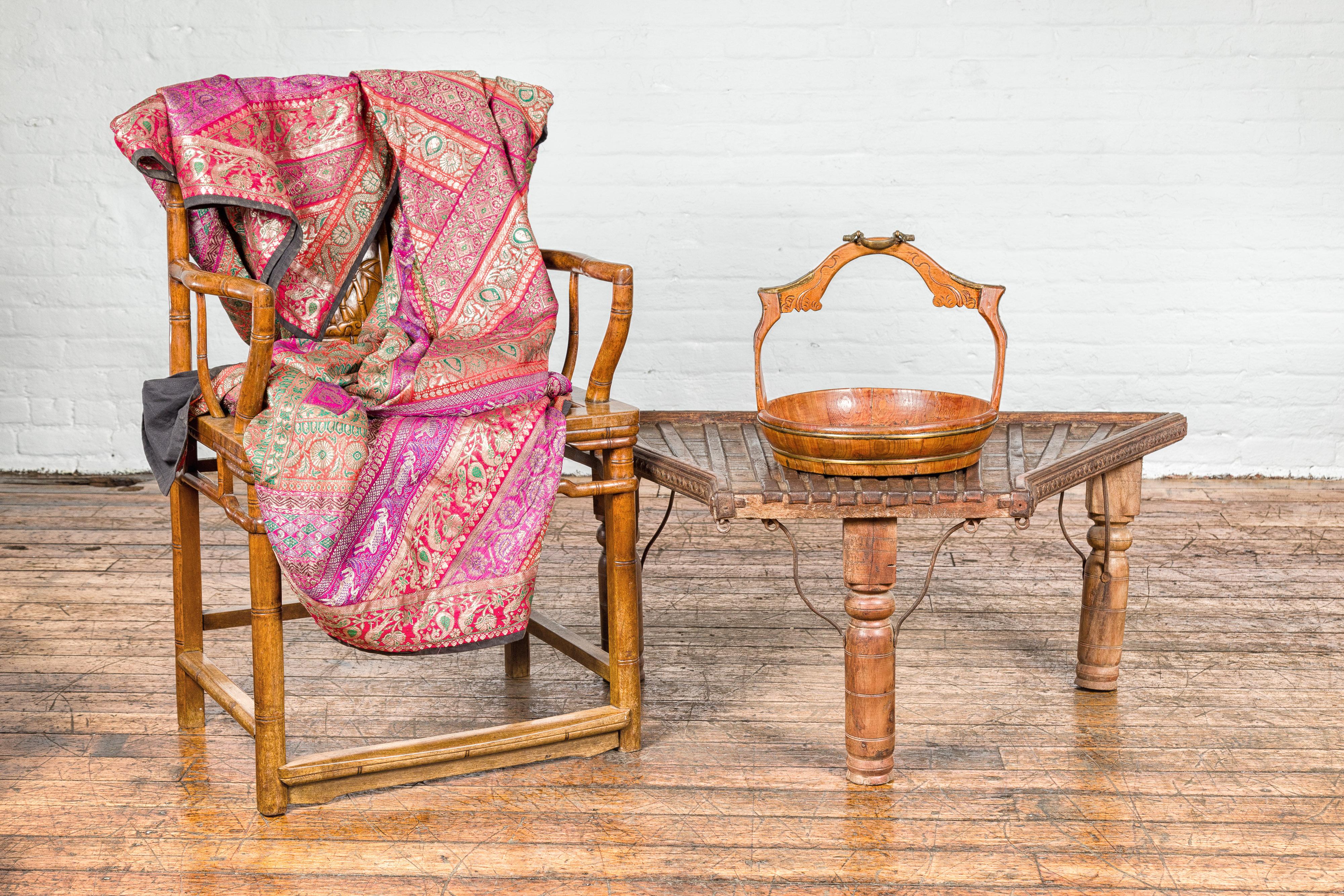 Ancienne table basse rustique faite à la main en Inde, avec un plateau trapézoïdal, une façade en saillie, des traverses en fer incurvées, des pieds balustres tournés et une patine joliment altérée par les intempéries. Cette table basse indienne
