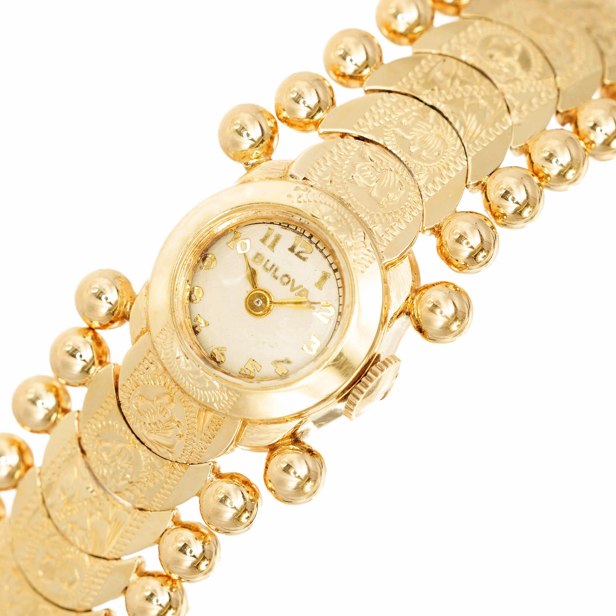 Damen 14k Gelbgold Bulova Armbanduhr. Das Armband besteht aus floral geprägten Gliedern mit einer 4 mm großen Goldkugel auf jeder Seite. 10.5 mm Lünette mit weißem Zifferblatt, goldenen Zahlen und Zifferblättern. Enthält eine Sicherheitskette in