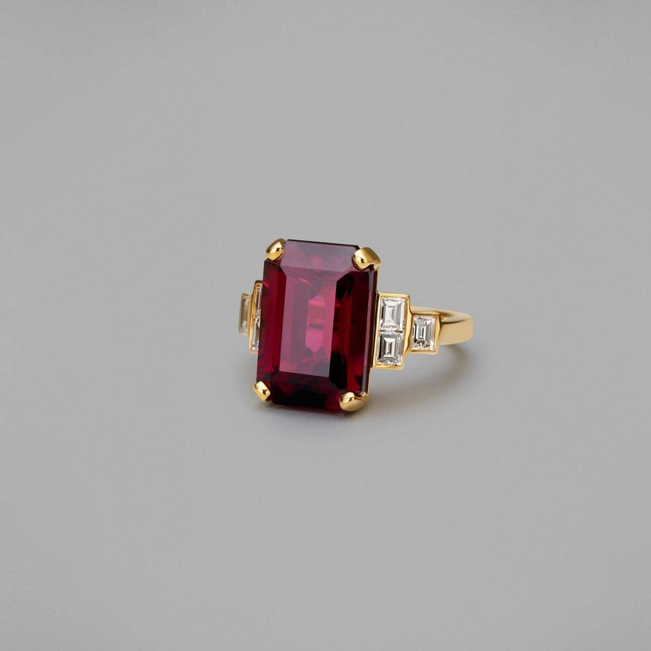 A BUNDA 'Volans' rhodolite garnet & diamond ring, set in 18 carat yellow gold, size M1/2, Signed BUNDA.

Characteristics of Purple Emerald cut Garnet; = 14.51ct.

Characteristics of Additional Baguette Cut Diamonds: 6 = 0.90ct, F colour, VS