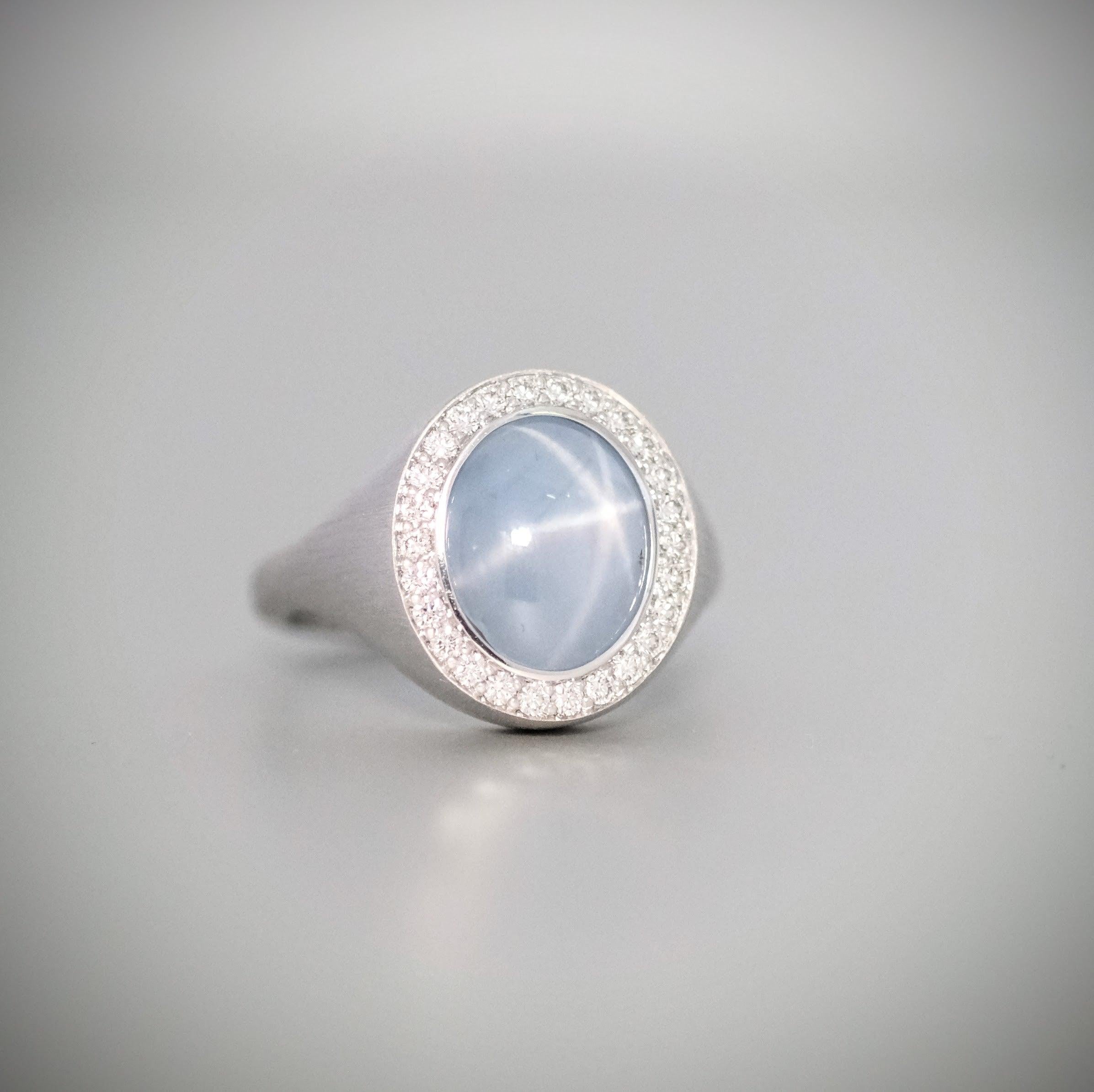 Ein BUNDA Corvus Ring, besetzt mit einem Sternsaphir aus 18 Karat gebürstetem Weißgold. 
Unterzeichnet BUNDA.

Merkmale des Sternsaphirs: Cabochon-Schliff, 7,26ct.

Merkmale der Diamanten: Runder Brillantschliff: 26 = 0,26ct, Farbe F, Reinheit VS.