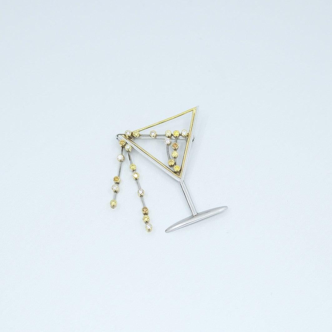 A BUNDA 'Couture' brooch in 18ct yellow gold and platinum, fetauring fancy coloured Argyle diamonds bezel set in the form of an overflowing martini glass, the diamonds range in colour, from fancy yellow, orange, pink to bluish grey.

Weight of