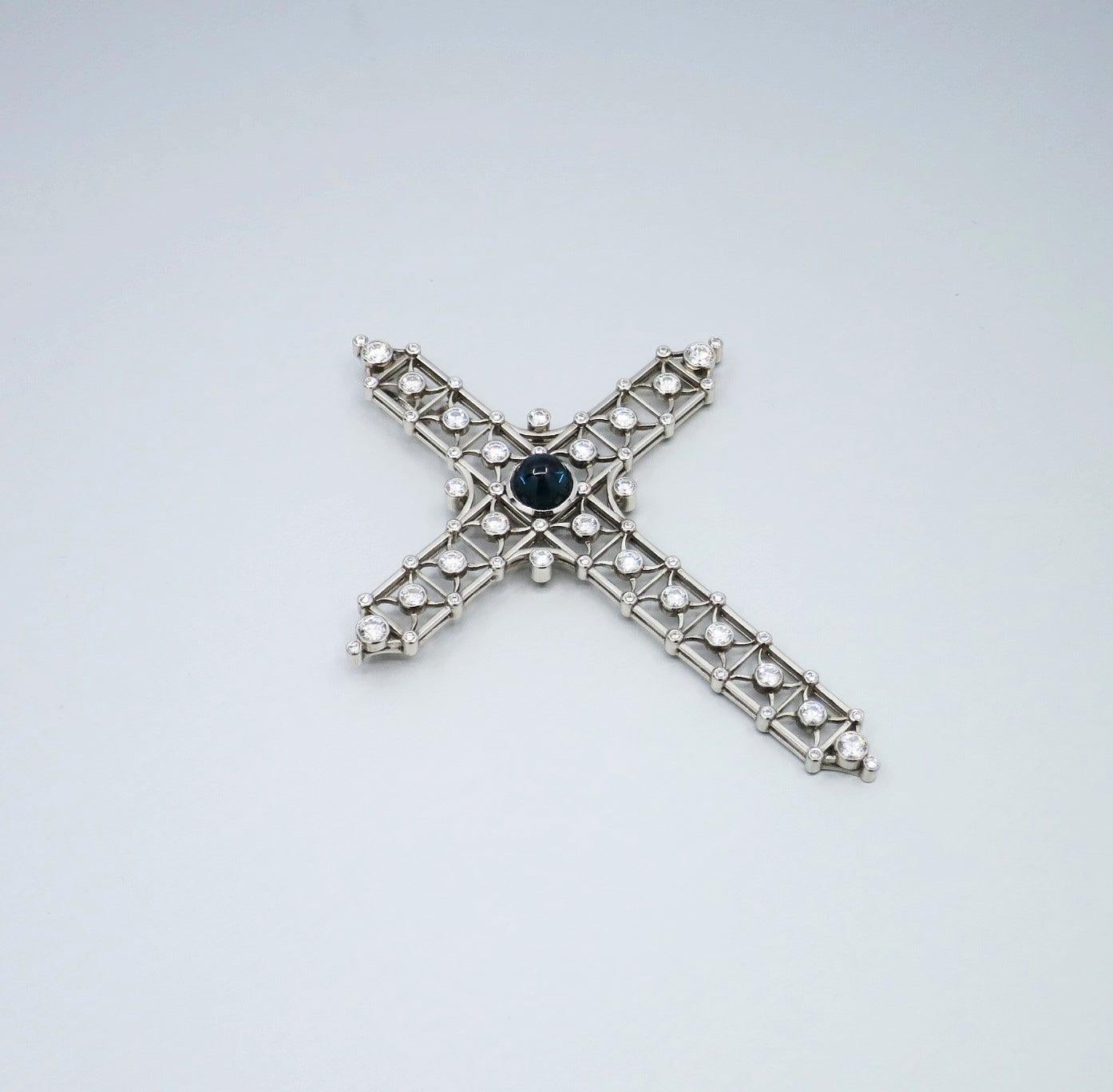 A BUNDA sapphire and diamond 'Cross' pendant in platinum, featuring a blue cabochon cut sapphire, bezel set to the centre and round brilliant cut diamonds bezel set amongst open relief work.

Characteristics of sapphire: 1 = 2.84ct.

Characteristics