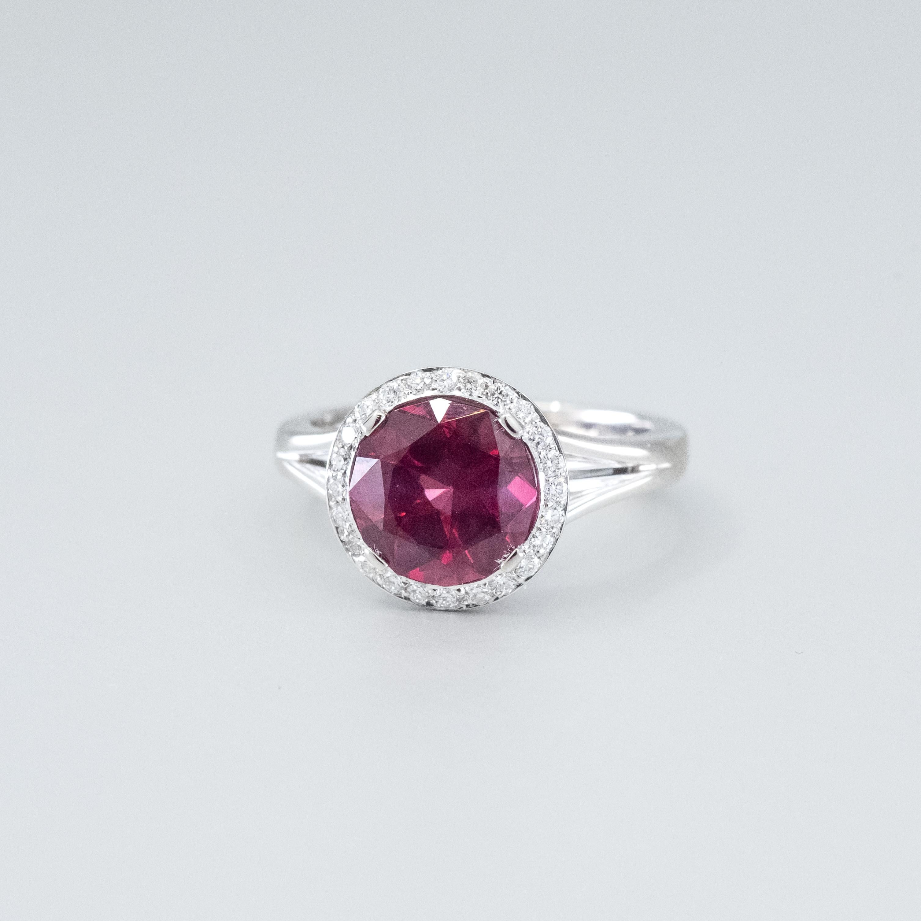 A BUNDA 'Sitara' ring in platinum. The ring is set with a rhodolite garnet in a four claw setting with a thread-set diamond halo, in platinum. Stamped BUNDA.

Characteristics of Red Round Brilliant cut Garnet; 1 = 3.24ct. C

Characteristics of