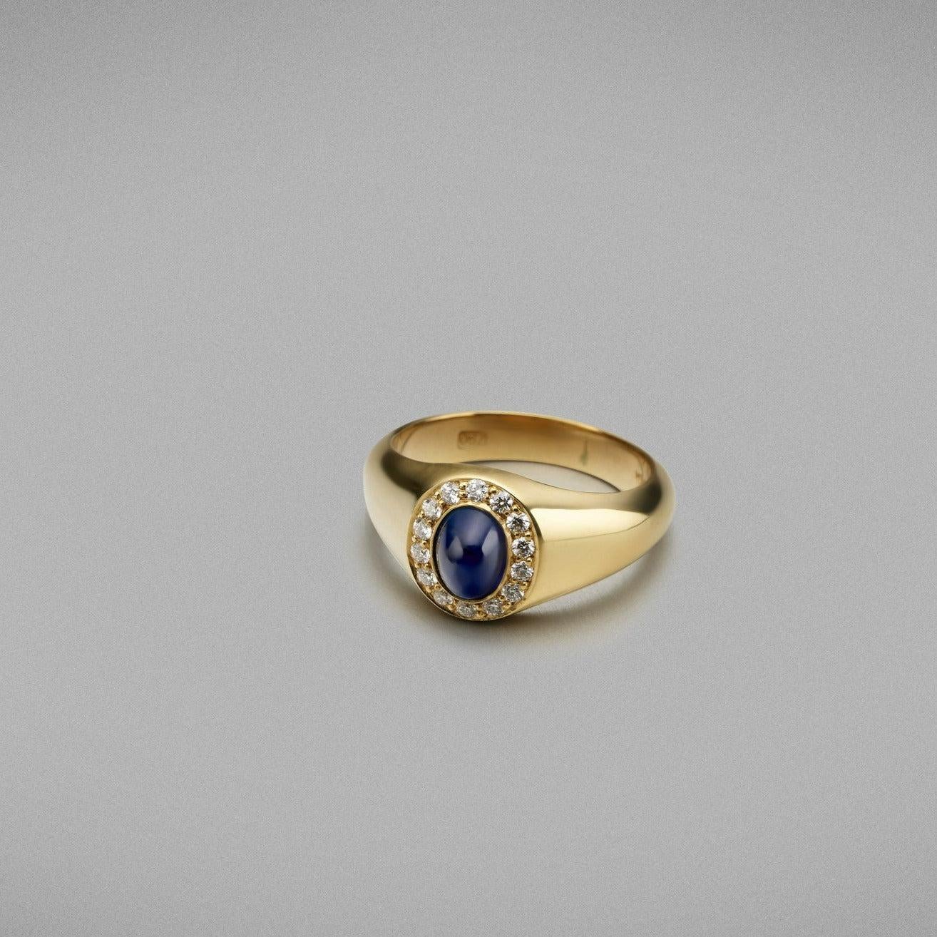 A BUNDA 'Signet' ring in 18ct yellow gold set with a cabochon cut Sapphire and a thread set diamond halo.

Characteristics of cabochon cut Sapphire: =1.10ct

Characteristics of additional diamond: 14 = 0.16cts, F/VS Clarity.

Total weight: 7.19g