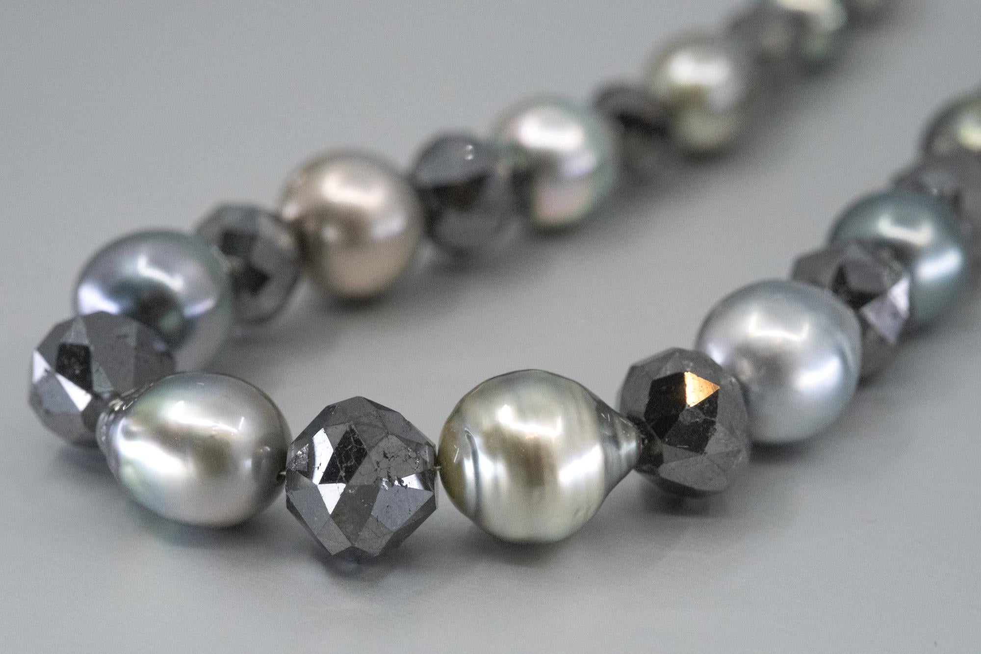 A BUNDA Pearl and Diamond Strand, featuring 34 Tahitian pearls, of round to Baroque shape between
8-11.8mm and 11 faceted black diamonds, on an 18ct yellow gold knot-shaped clasp. 
Characteristics of the Tahitian Pearls: 34 pearls in totals. 
 