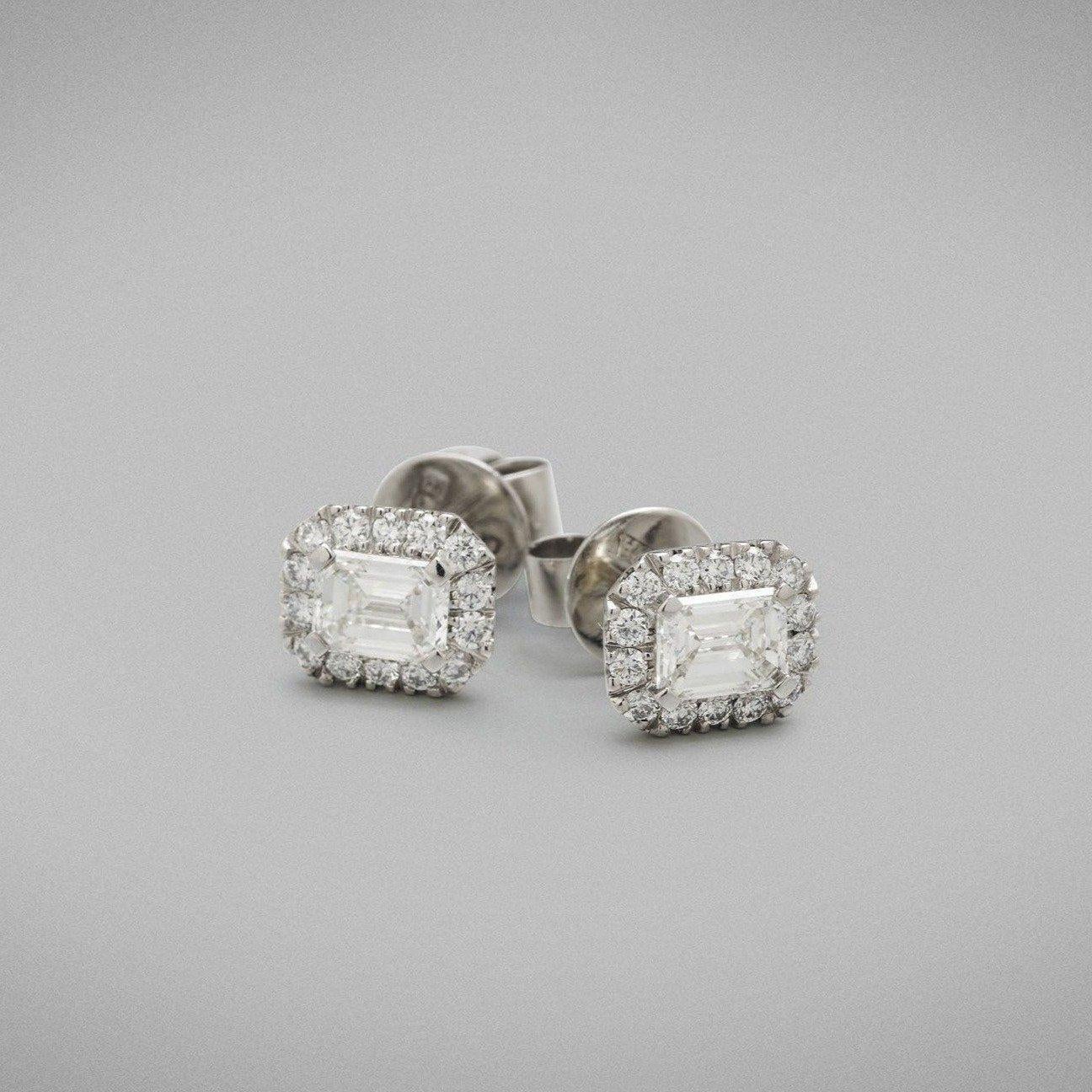 A pair of BUNDA 'Valentin' diamond earrings in white gold. Each earring is set with an emerald cut diamond in a four claw setting, with round brilliant diamonds castle-set to the head. Fittings are post and butterfly in platinum - Butterflies are
