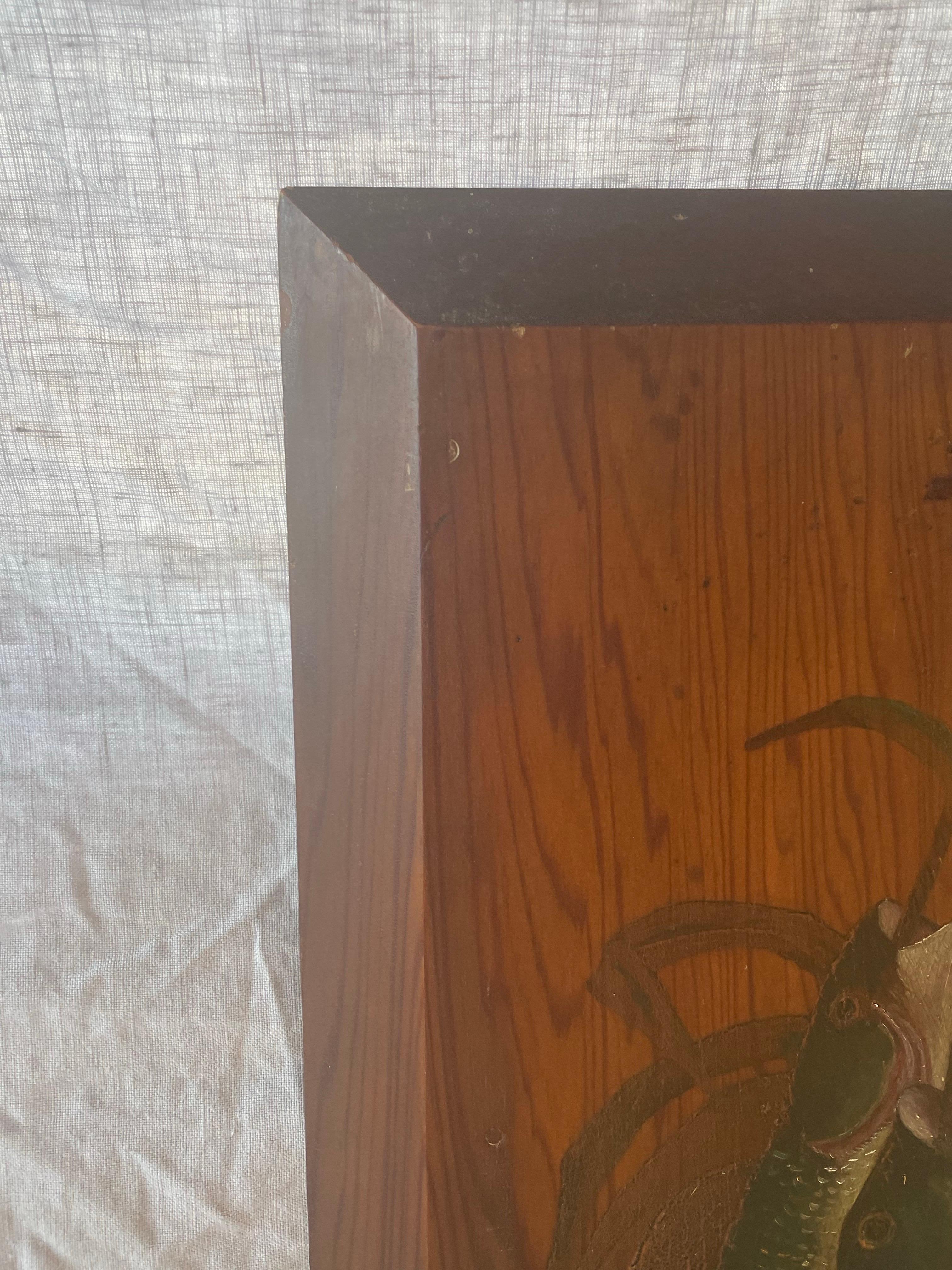 Une peinture à l'huile habilement exécutée représentant un trio de poissons fraîchement pêchés suspendus à des roseaux, rendue directement sur un panneau de bois richement grainé. L'artiste a tiré parti du motif naturel du bois dans le cadre de la