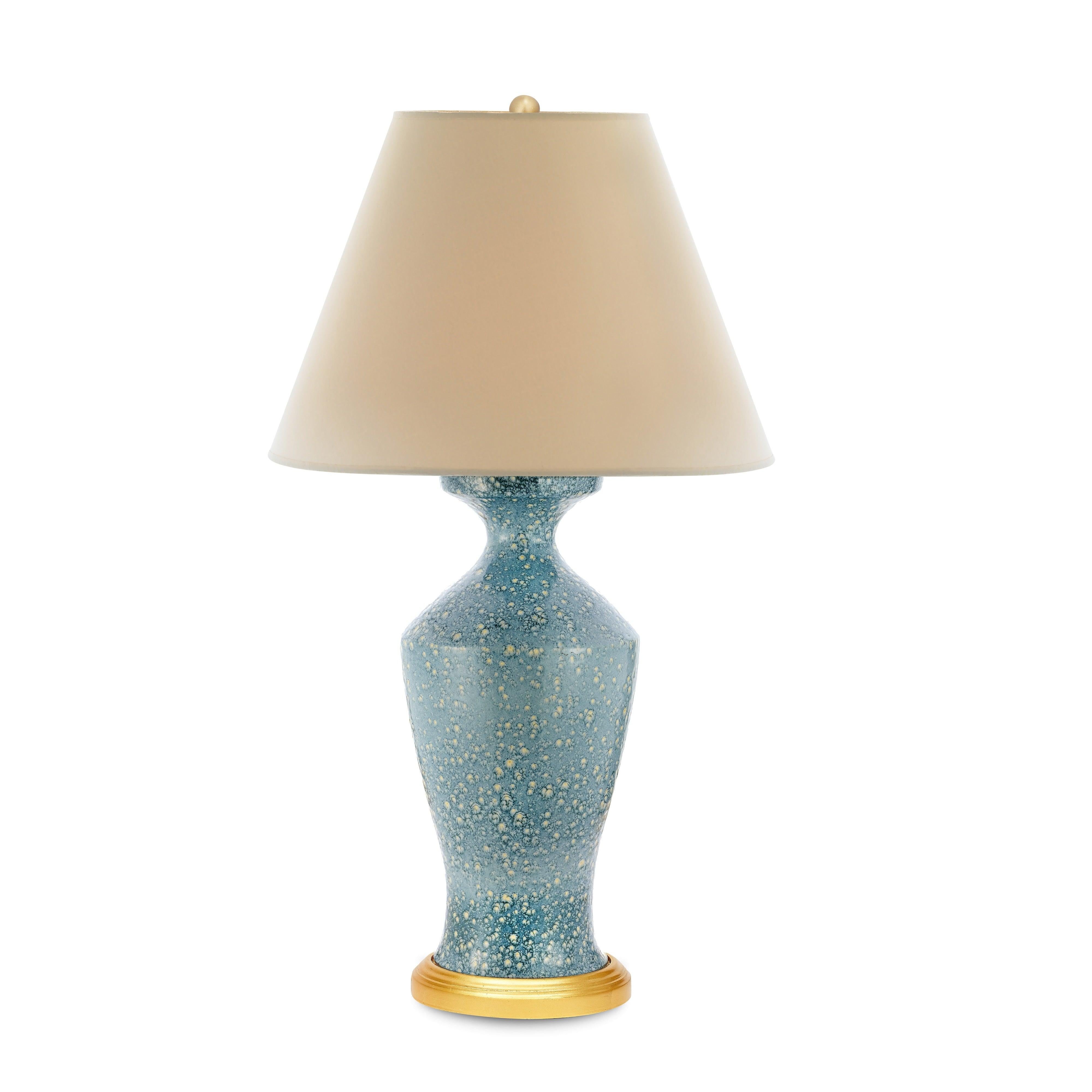 A mesmerizing mix of color and texture, the Celestine Lamp is a true statement piece. Its classic urn-shaped ceramic base is finished in a rich blue reactive glaze that creates an overall speckled effect. Resting on a gilded base, this lamp brings