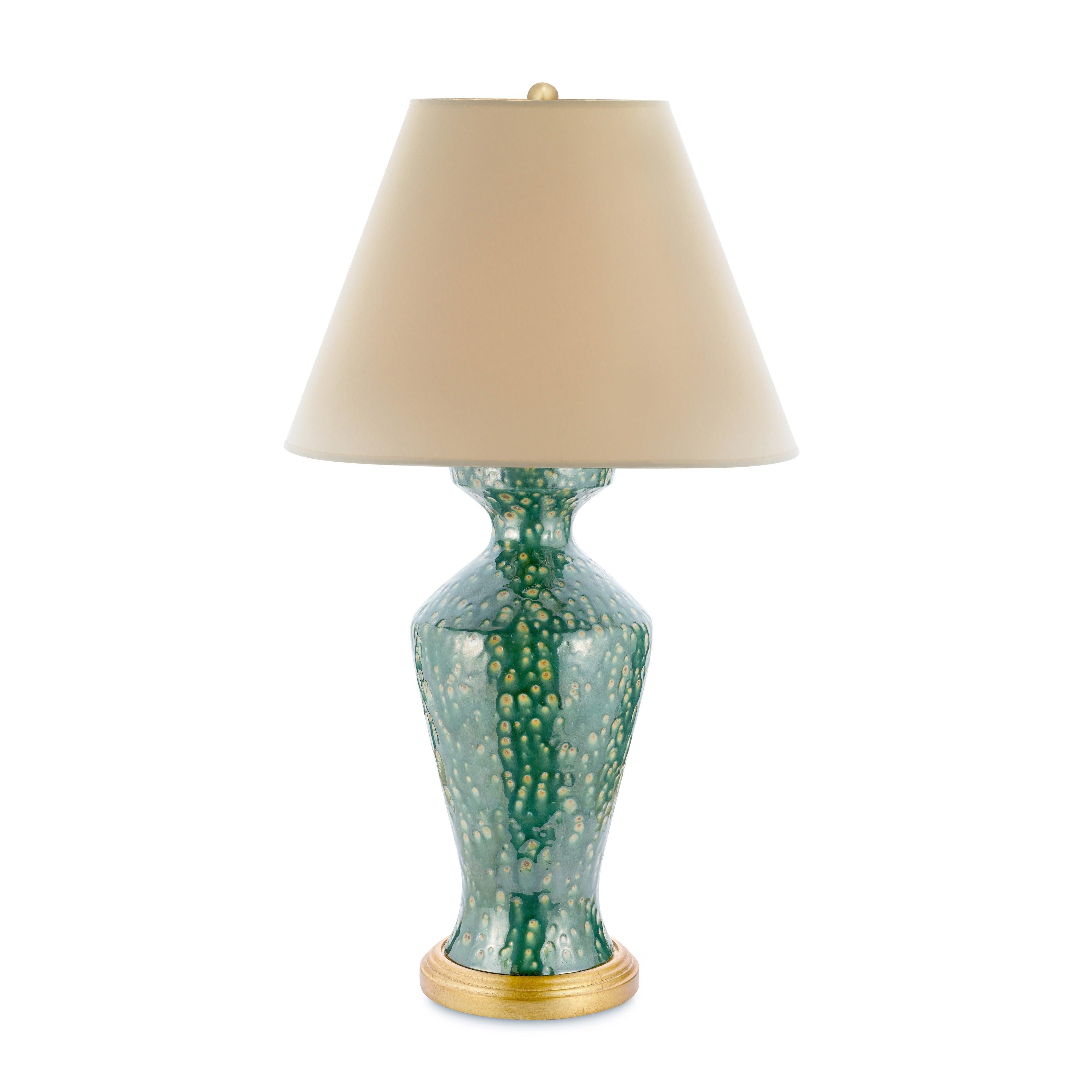 A mesmerizing mix of color and texture, the Lagoon Lamp is a true statement piece. Its classic urn-shaped ceramic base is finished in a rich green reactive glaze that creates an overall speckled effect. Resting on a gilded base, this lamp brings an