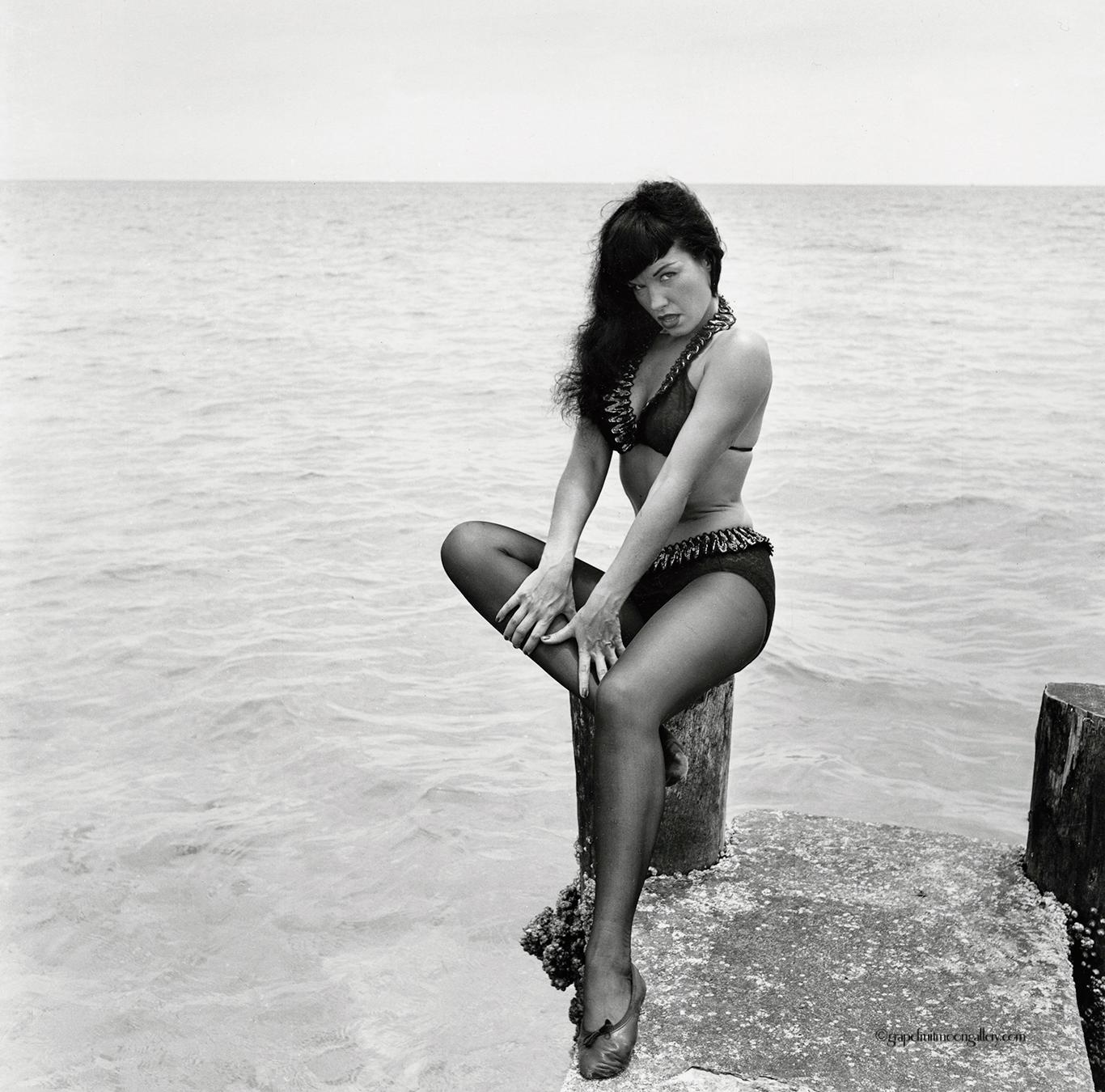 Bunny Yeager Black and White Photograph - Bettie Page Seated on Pier
