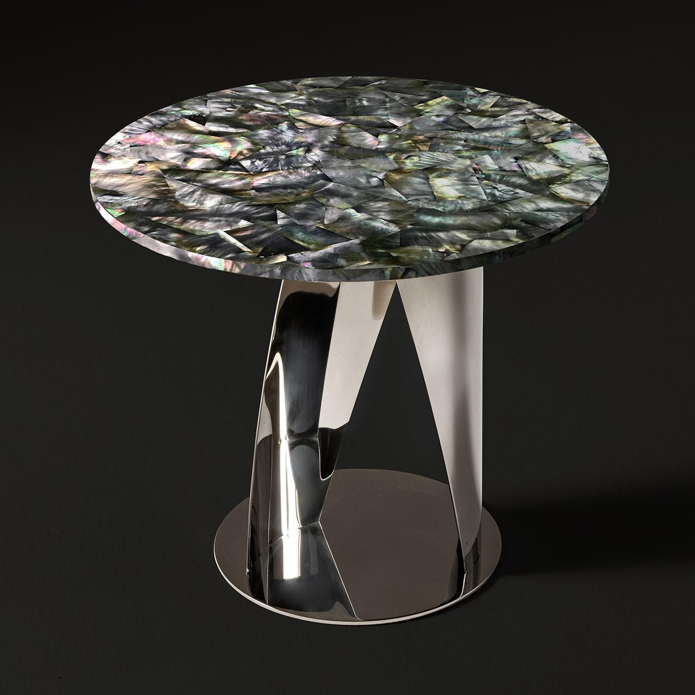 In this superb side table, curved and slightly twisted metal sheets extending from a coordinated disk base guide the eye to its lustrous round top in prized black nacre. Offered in a captivating galvanized chromed finish, the base distills pure