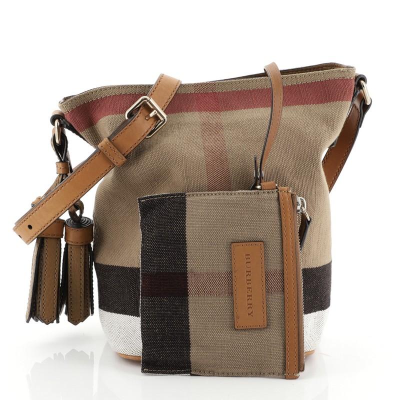 This Burberry Ashby Handbag House Check Canvas Mini, crafted in neutral house check canvas, features a single looped leather handle, leather tassel and trim, and gold-tone hardware. Its magnetic snap closure opens to a neutral fabric interior.