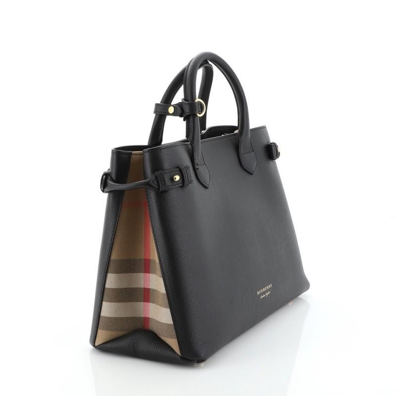 This Burberry Banner Convertible Tote Leather and House Check Canvas Medium, crafted in black leather and house check canvas, features dual rolled handles, stamped Burberry logo, and gold-tone hardware. Its magnetic snap closure opens to a black