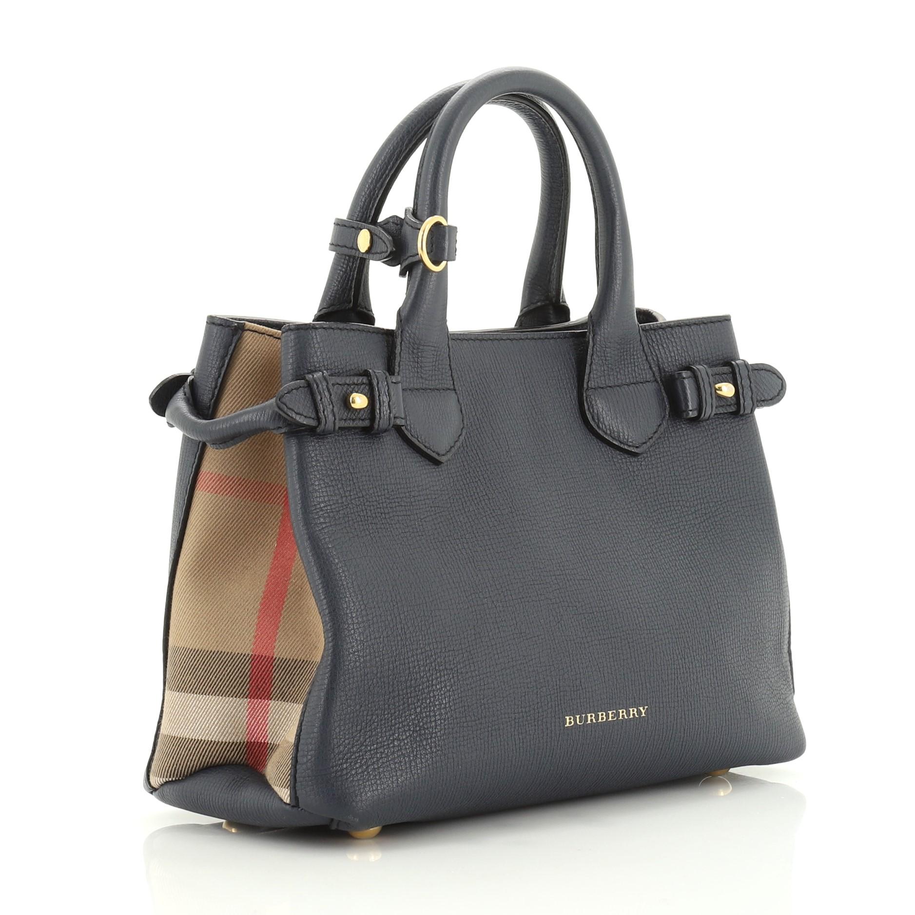 This Burberry Banner Convertible Tote Leather and House Check Canvas Small, crafted in blue leather and house check canvas, features dual rolled handles, house check canvas side panels, protective base studs and gold-tone hardware. Its magnetic snap