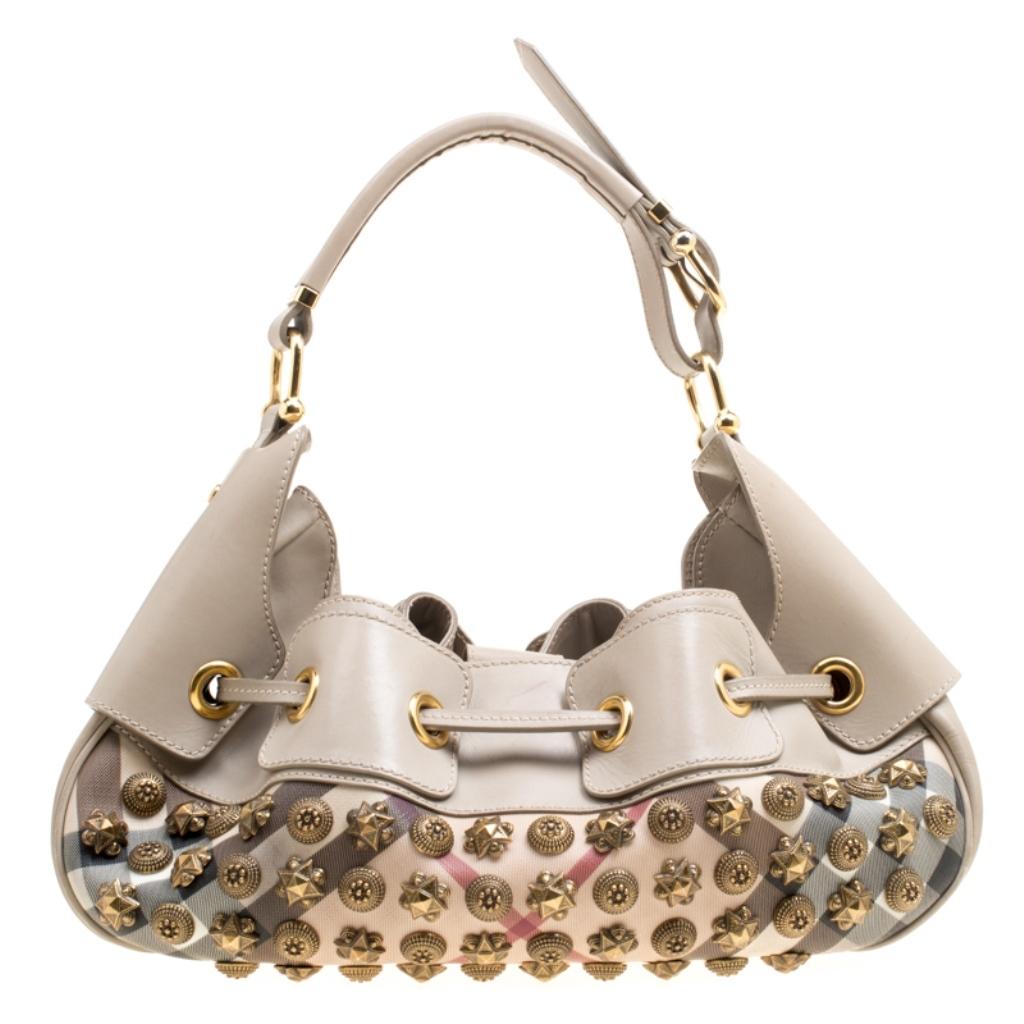 This Burberry Warrior hobo will make a splendid addition to your bag collection. It is crafted from PVC and leather and designed with multiple studs in their signature Super Nova check. The bag has a drawstring top and a nylon interior that is