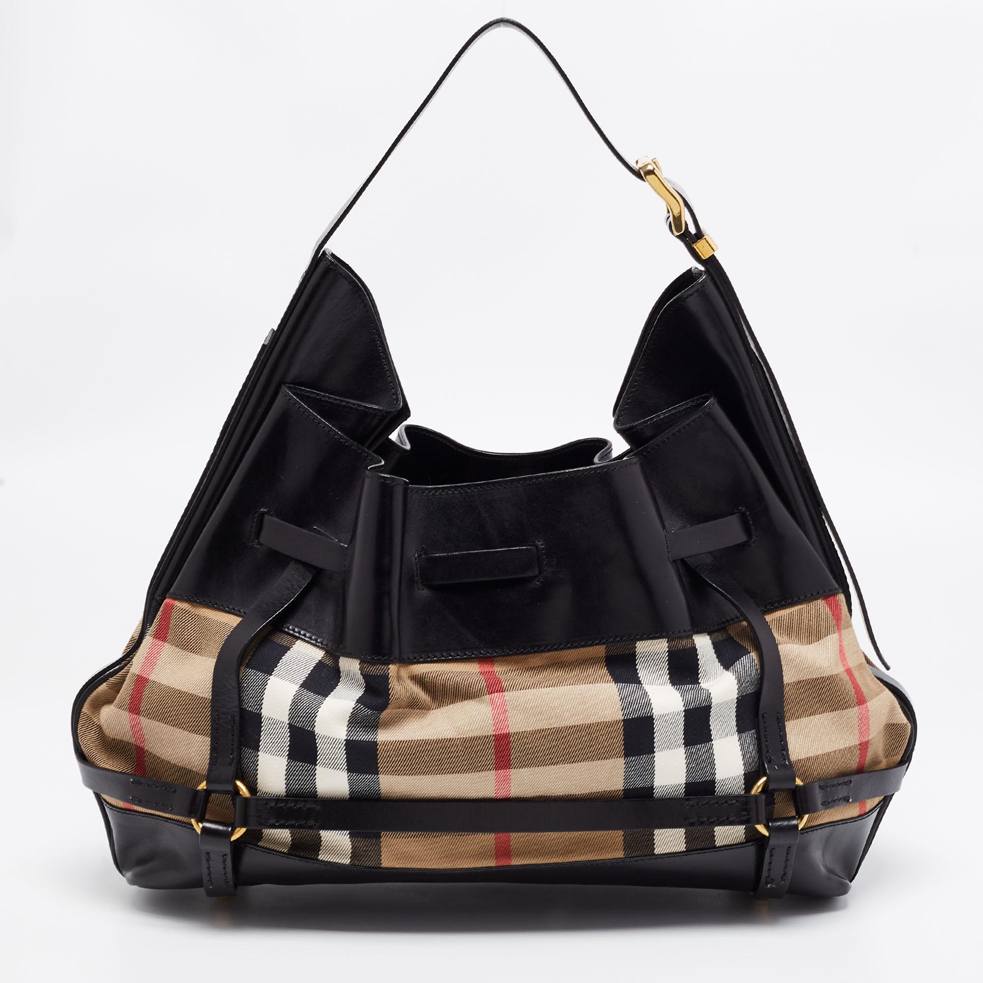 This stylish and functional hobo comes from the house of Burberry. Crafted in Italy, this bag has been made from leather and House Check canvas. It is styled with a single handle, buckled straps, and gold-tone hardware. It opens to a canvas interior