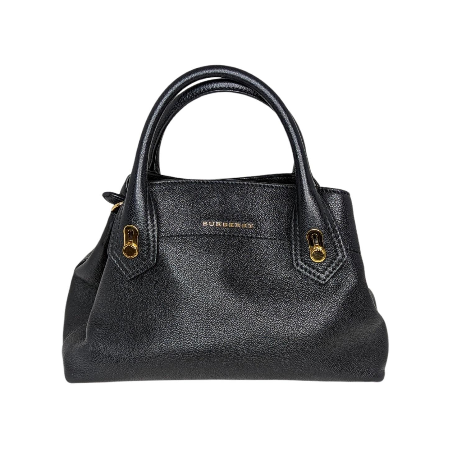 This stylish tote is beautifully crafted of pebbled calfskin leather in black. The bag features a black leather shoulder strap, a black leather top handles and gold hardware. The handbag opens to a house check with a flat pocket and central zipper