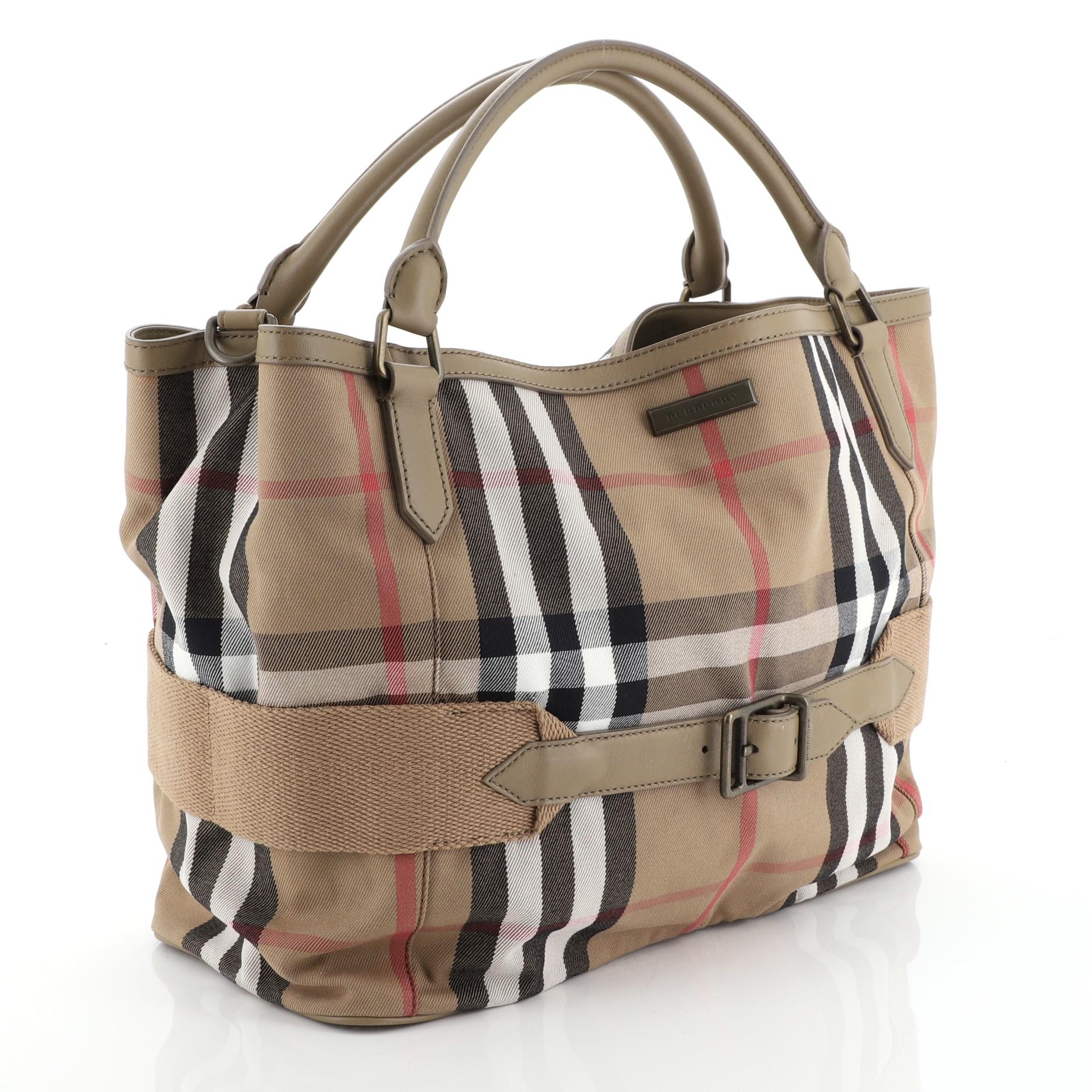 This Burberry Brecon Convertible Tote House Check Canvas, crafted from neutral Burberry canvas, features dual-rolled leather handles, detachable buckle shoulder strap, utilitarian grosgrain belt, Burberry logo plate at front, and aged gold-tone