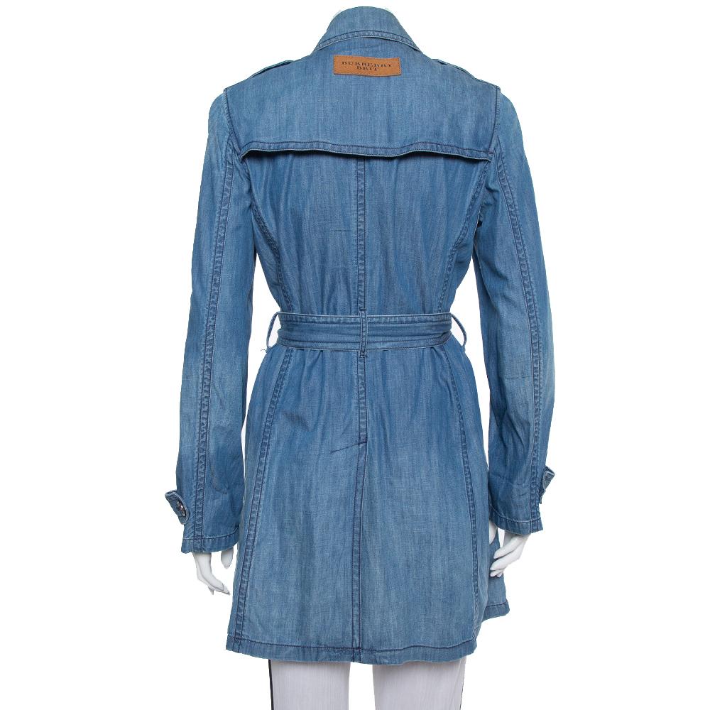 Burberry is known for its trench coats. This creation exudes elegance and is great for casual wear. Crafted from denim fabric, this trench coat comes in blue color. It features a simple collar, button closure, two external pockets, a belt that rests